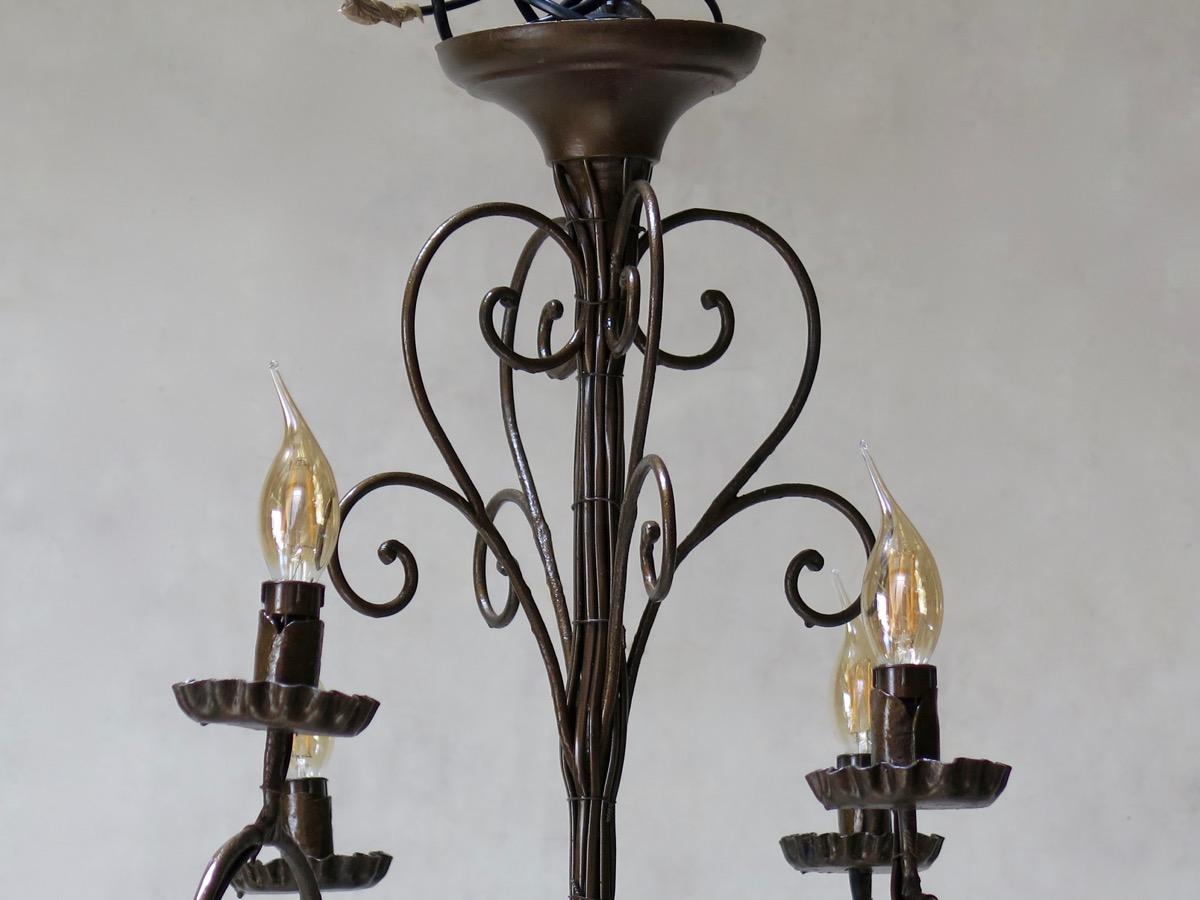 Grand lustre à huit lumières en fer, avec une finition or bruni. Bras et détails à volutes élaborées, se terminant par un fleuron.