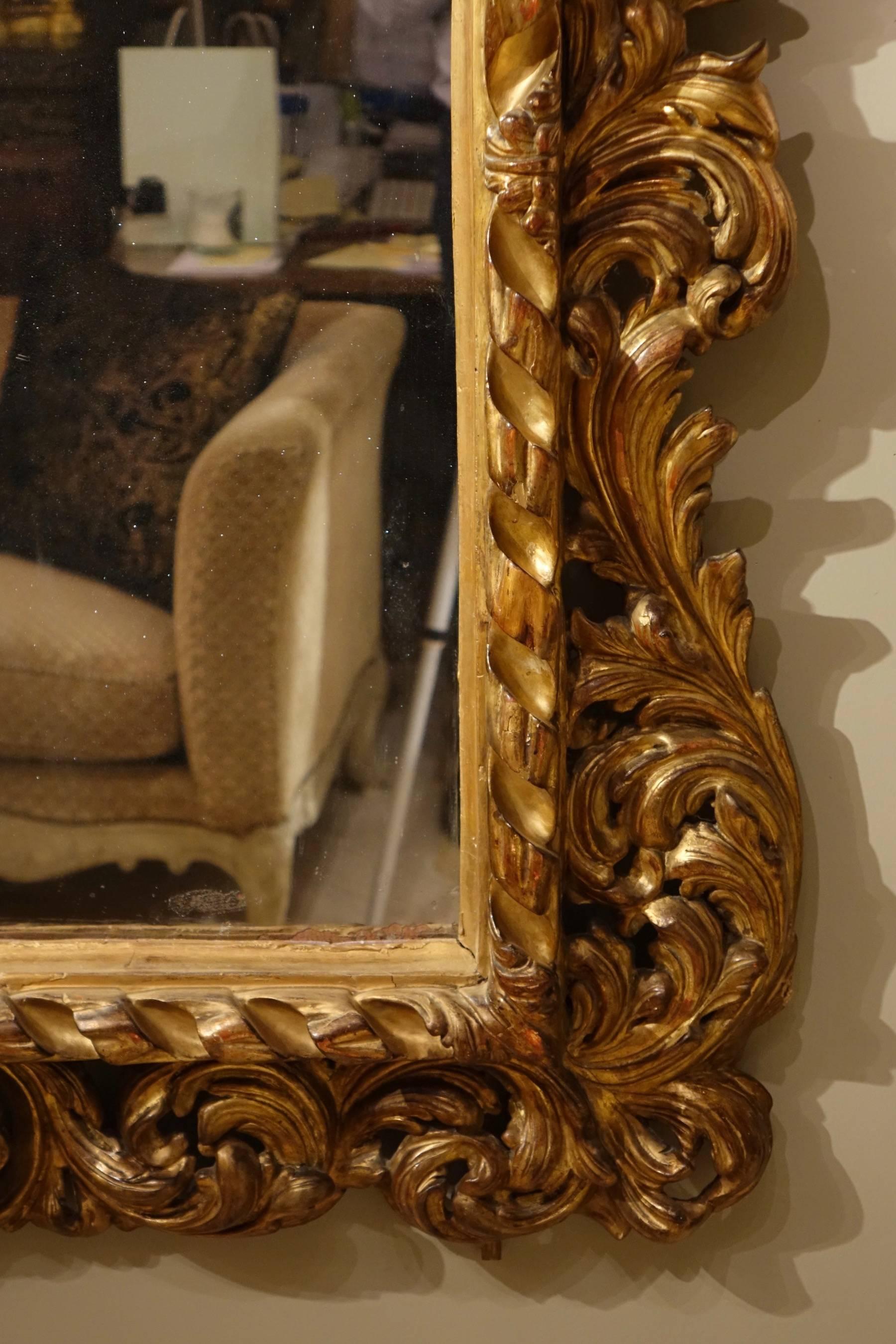 18th century Italian large carved and gilt wood mirror with pediment representing an inverted shell. Carved with curls of foliage. Mercury stain glass.
Wear and tear on gilt.
 