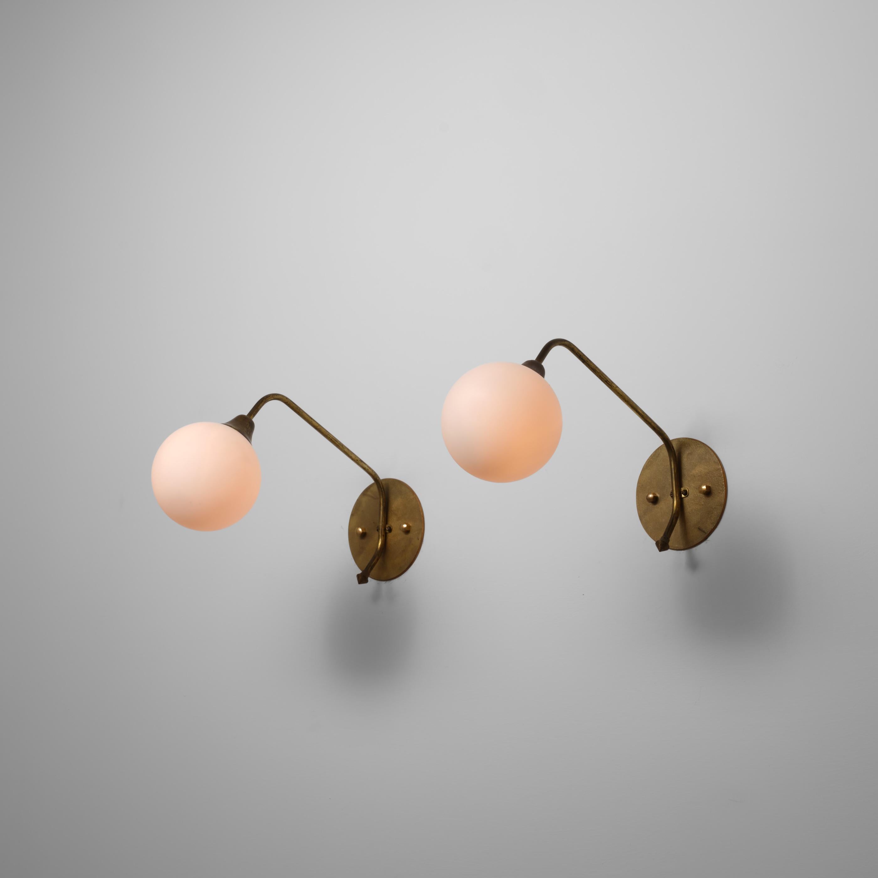 Este par de grandes apliques italianos de los años 50 combina una silueta minimalista con materiales refinados. Cada lámpara presenta un brazo de latón suavemente curvado que se eleva desde una placa de pared circular y soporta una pantalla esférica