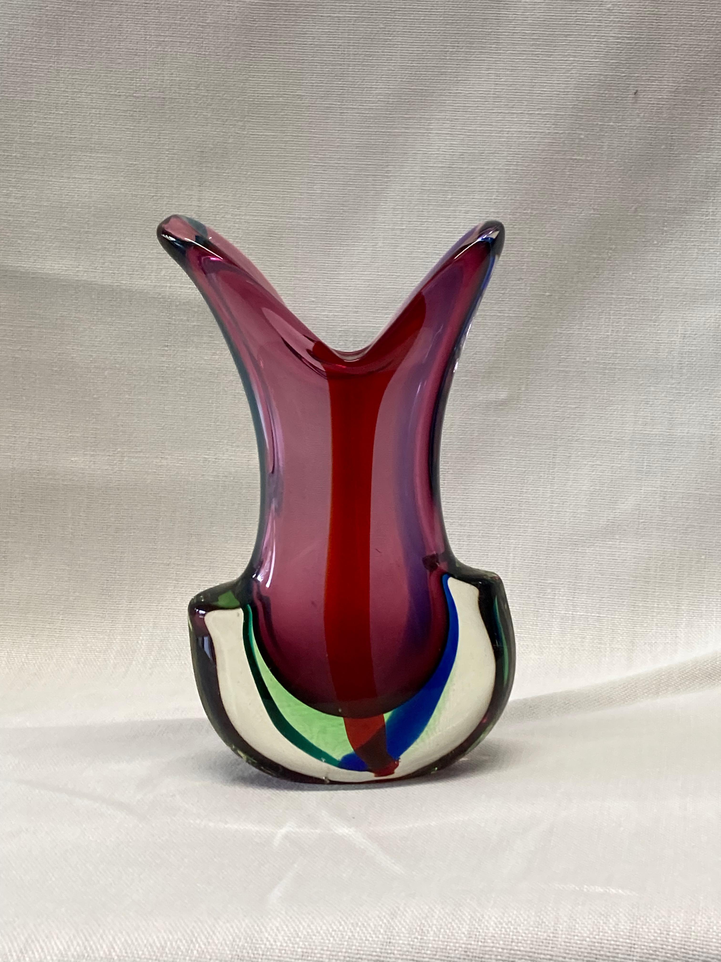 A large and heavy hand blown art glass vase from Murano Italy. Clear cased crystal glass with purple body and red, green, and blue accents.

Some of Venice's historical glass factories in Murano remain well known brands today, including De Biasi,