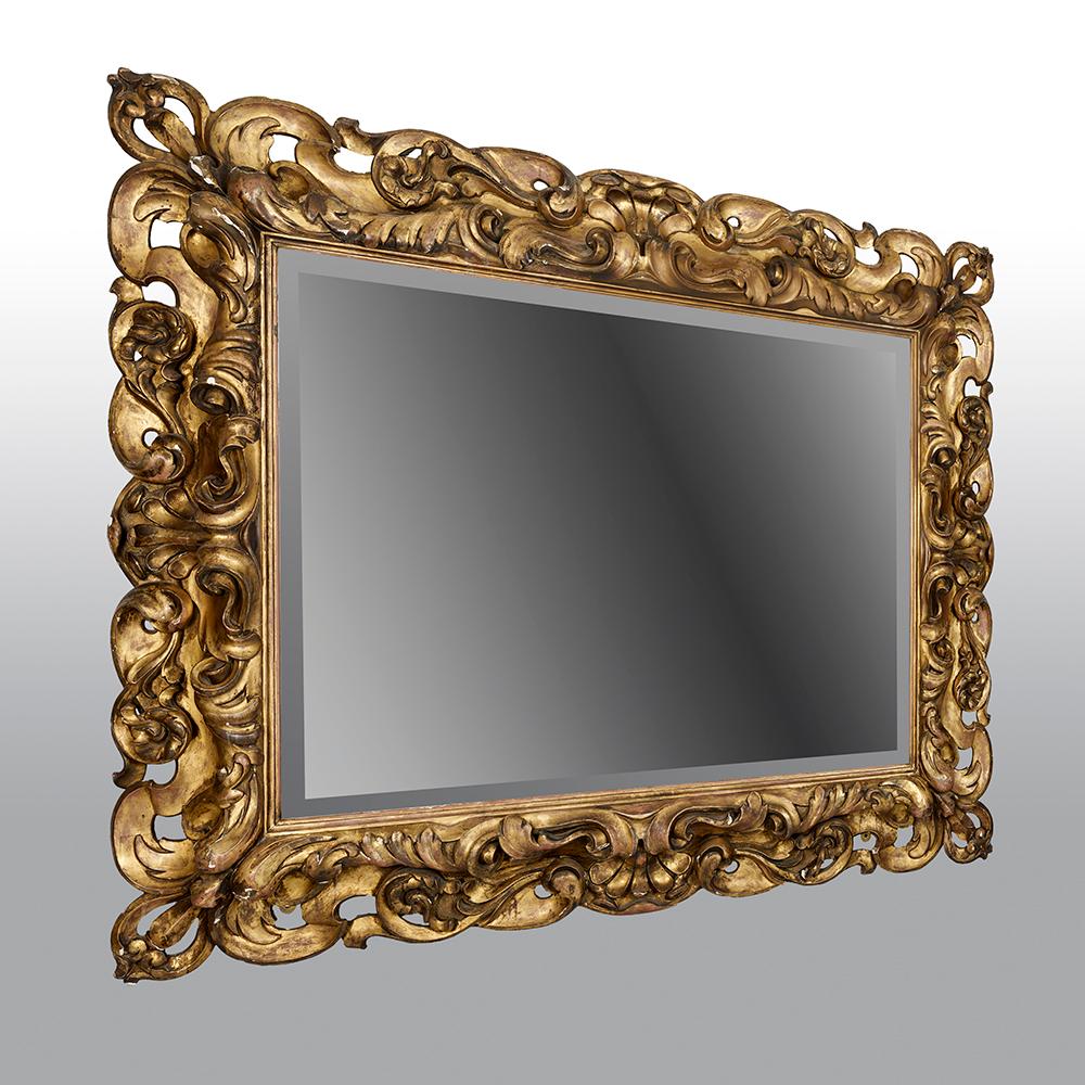 Questo specchio italiano in legno dorato intagliato di grandi dimensioni, risalente alla seconda metà del XIX secolo, presenta una cornice rettangolare in legno dorato riccamente intagliata, tipica del periodo rococò.