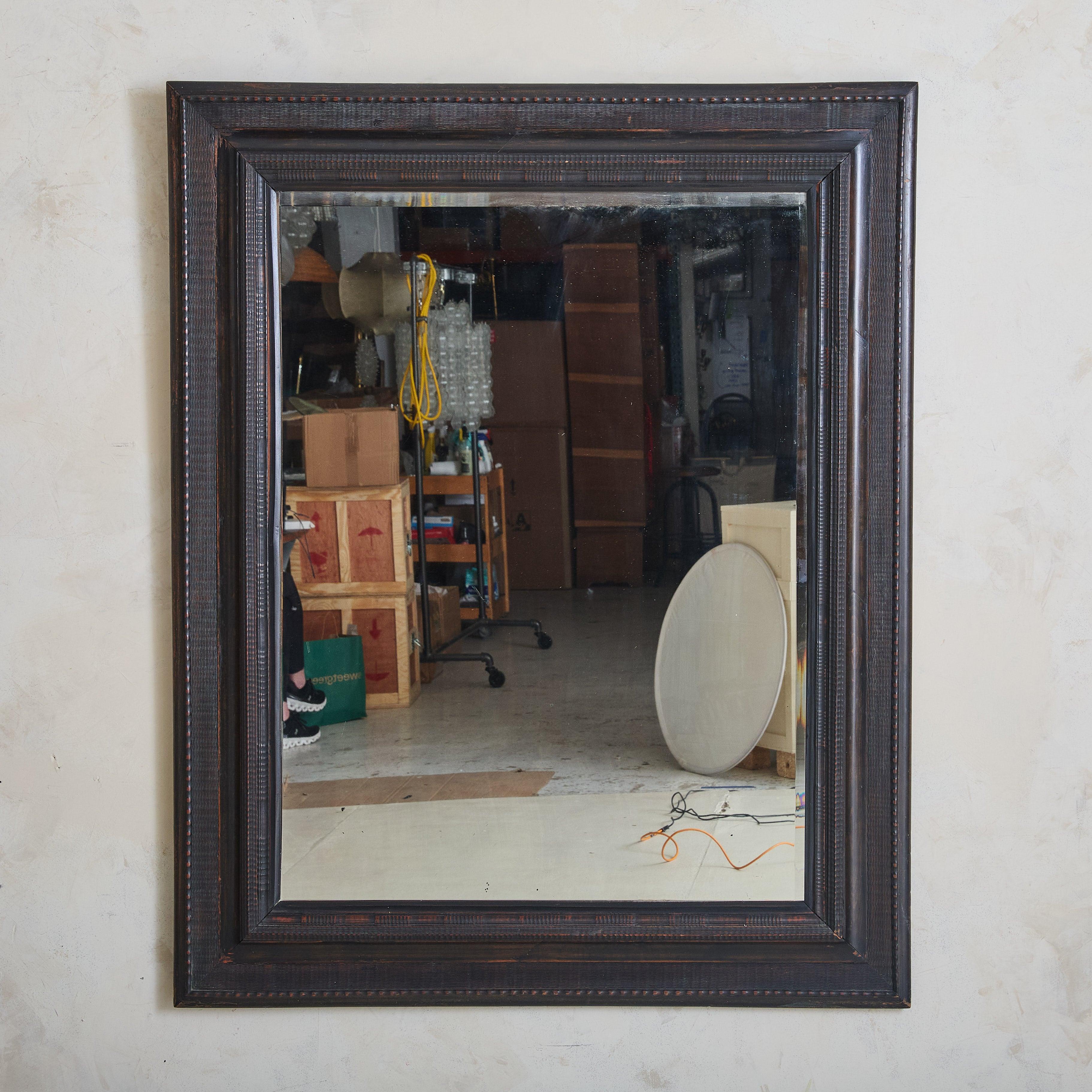 Crafted in Italy well over one hundred years ago, the black ebonized wooden frame of this striking mirror reflects 17th and 18th Century Dutch style. Its surface is intricately detailed and textured with carved patterns of indentations and