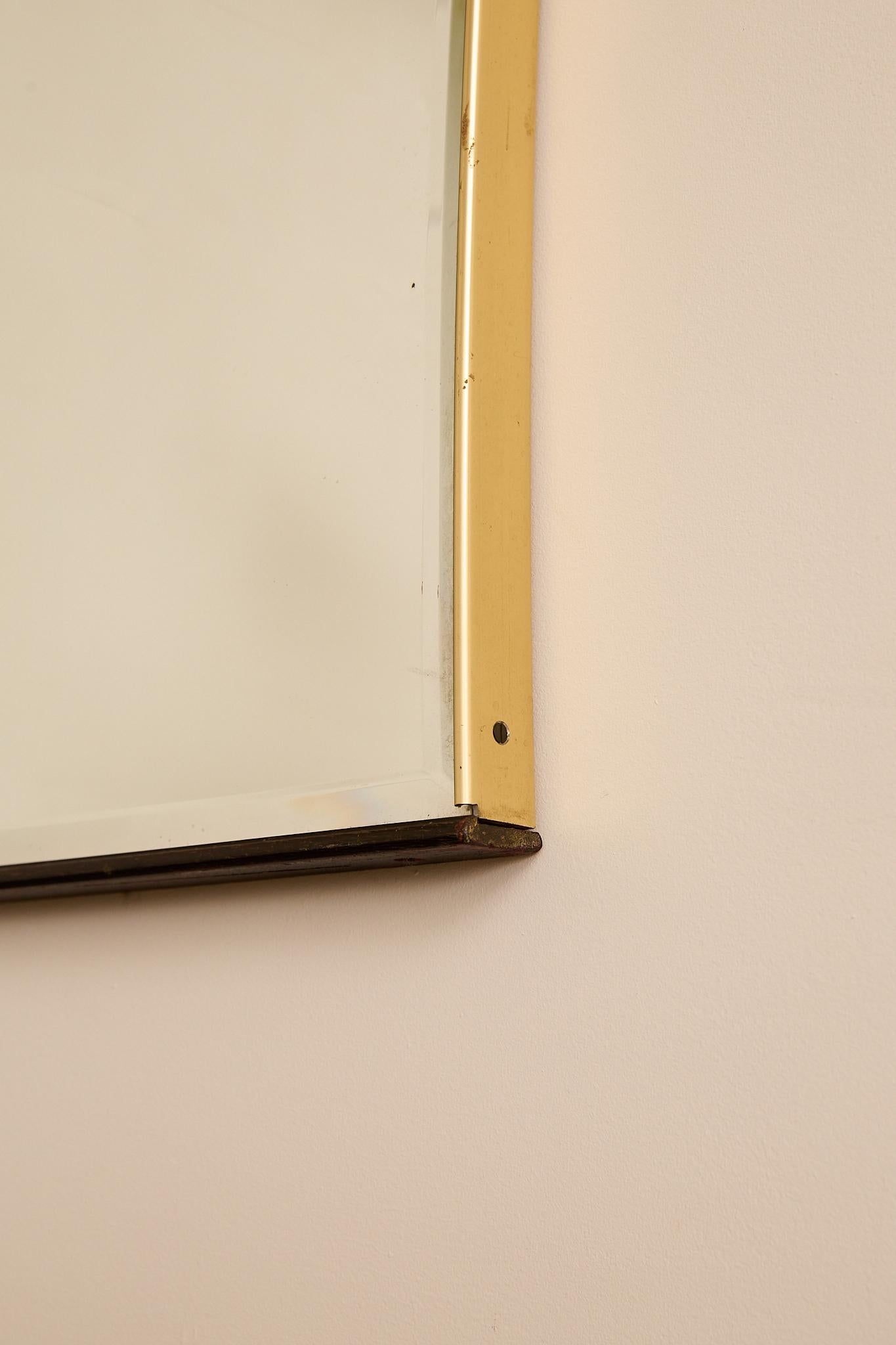 Large Italian wall mirror with a gently flared silhouette, framed in brass and finished with a dark wooden base rail. Subtle patina to the metal highlights its vintage character.