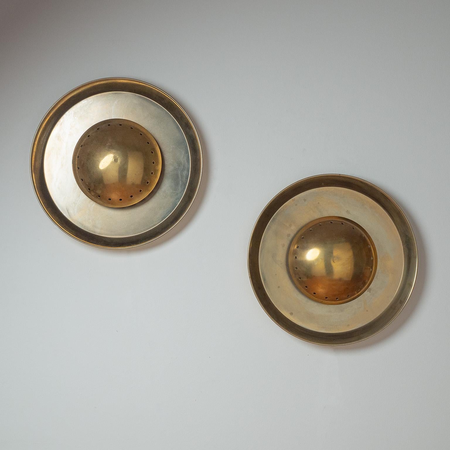 Fine pair of large Italian brass wall lights in the manner of Stilnovo. Large brass-plated steel backplate with a central perforated brass dome in the center, under which the two lights are positioned. Nice original condition with some patina on the