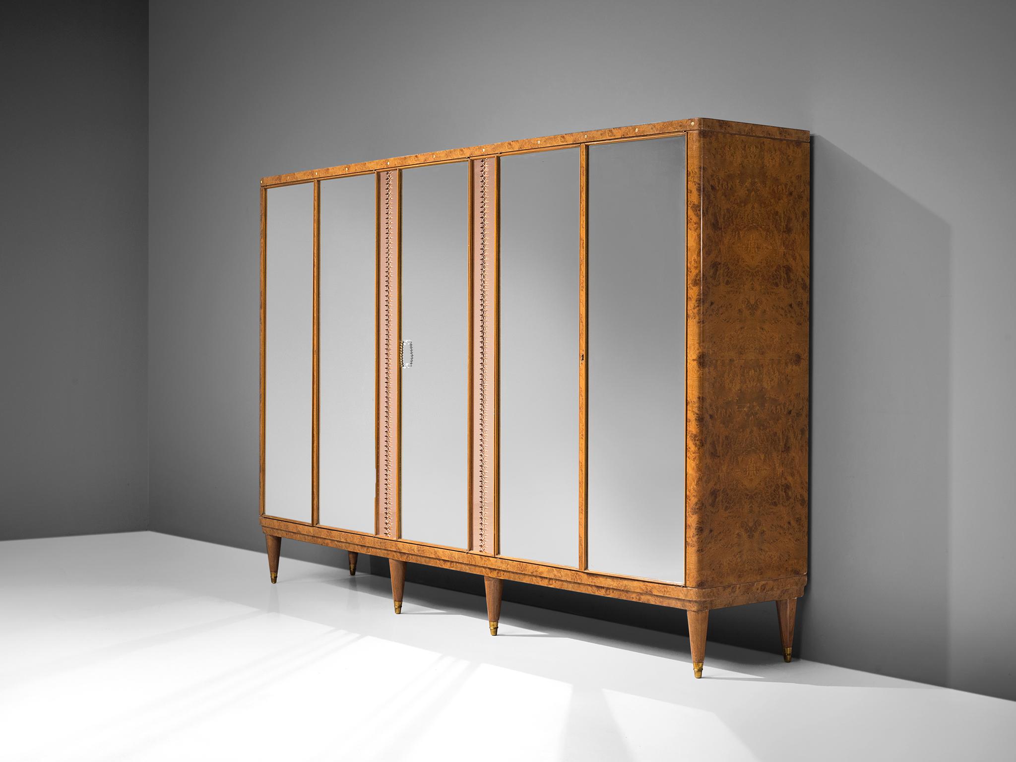 Cabinet, walnut burl, wood, glass, brass, Italy, 1940s.

This grand cabinet is executed in walnut burl, brass and pink glass rims. The cabinet features five mirrors behind which three sections are displayed. Surrounding the middle mirror there is