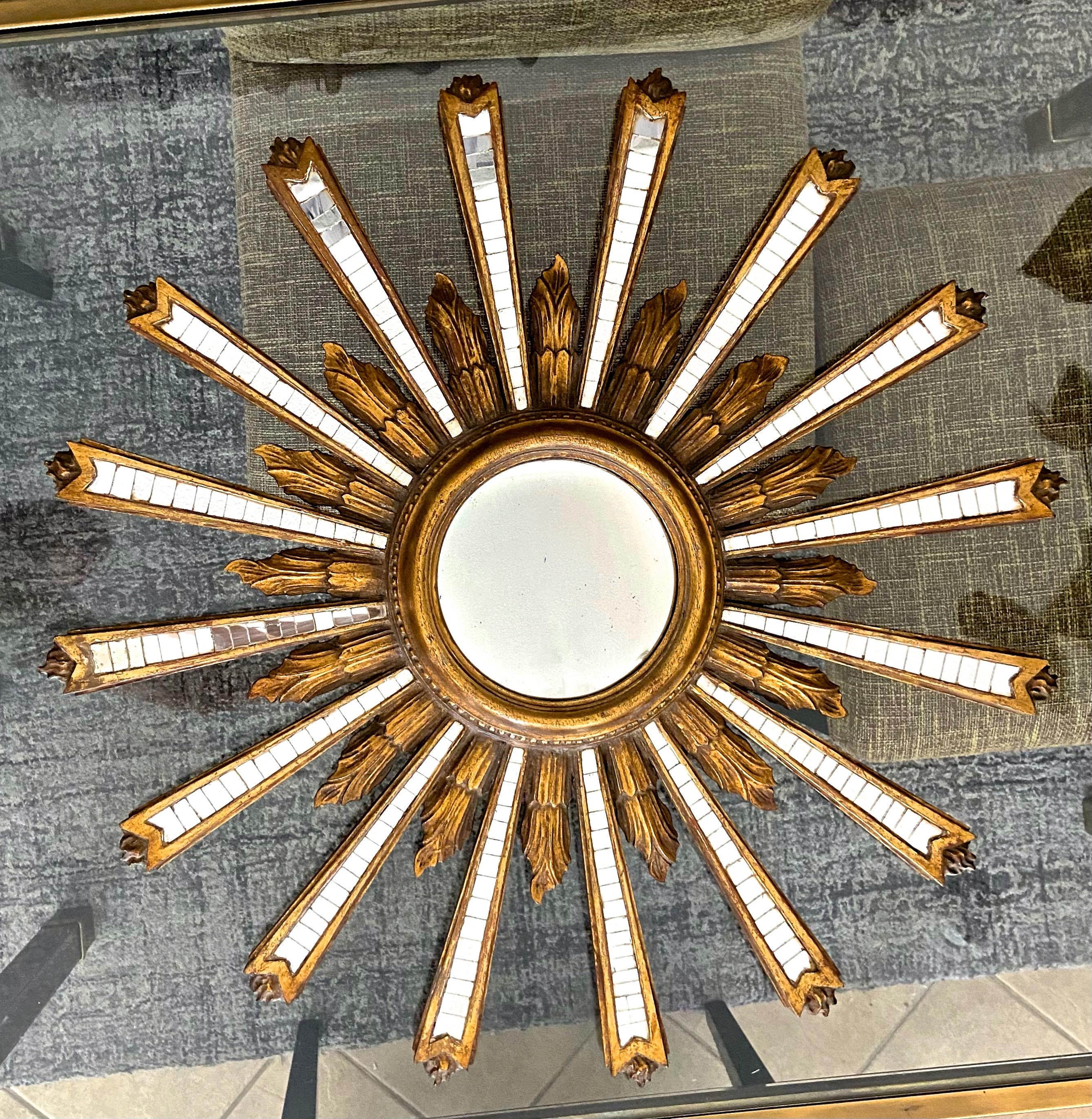 Large Italian hand carved gilt wood and gesso sunburst or starburst wall mirror with convex bulls eye center mirror. The round shaped mirror also features small inset pieces of mirror in each of the larger ray arms. The sunburst theme also includes