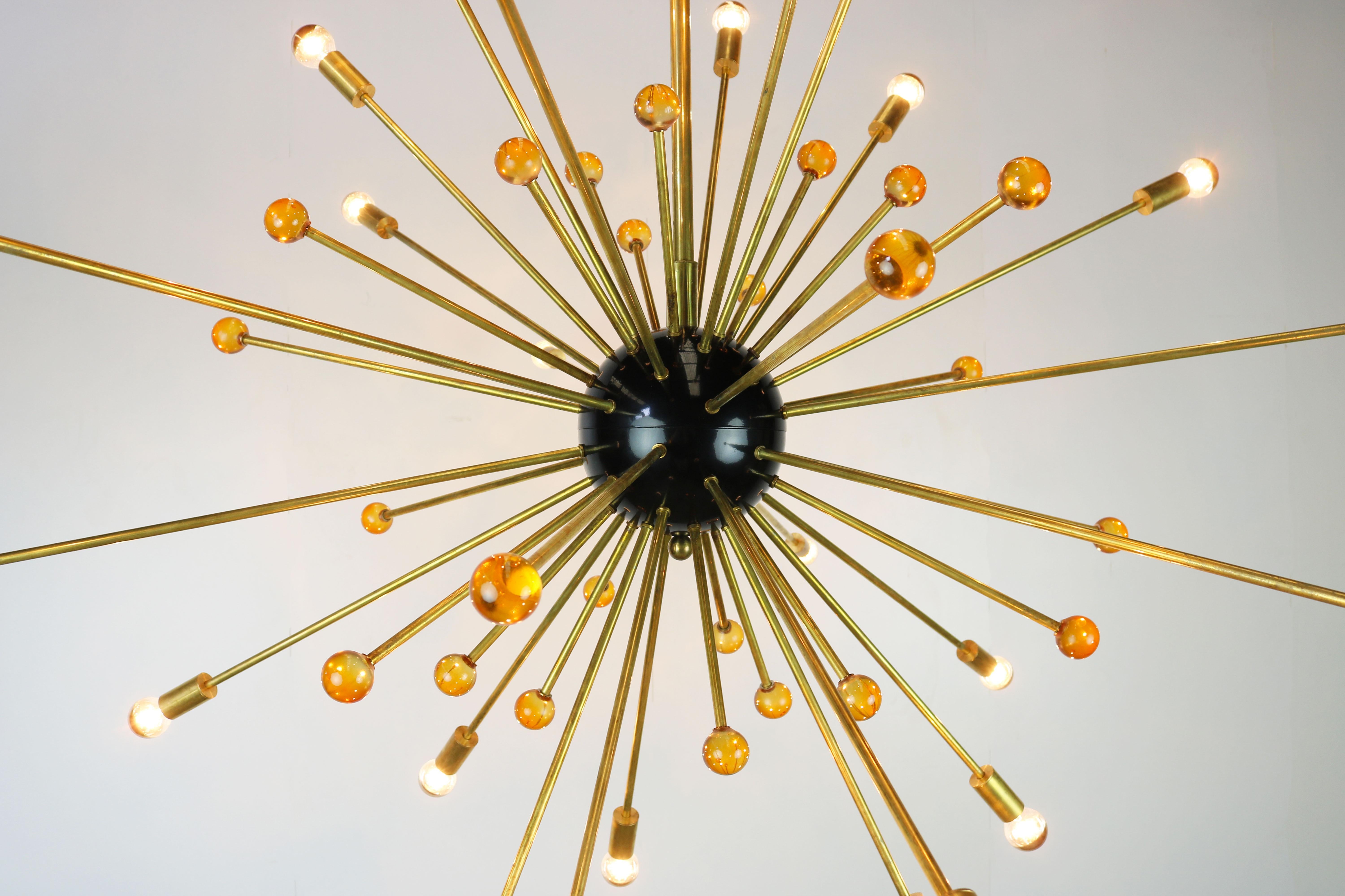 Lustre Sputnik massif Stilnovo d'un diamètre de 150 cm datant des années 1950. 
Le lustre est composé de 48 tiges en laiton, 24 tiges sont munies d'une douille et les autres 24 tiges sont munies d'une sphère en verre orange.
 Sa forme minimaliste
