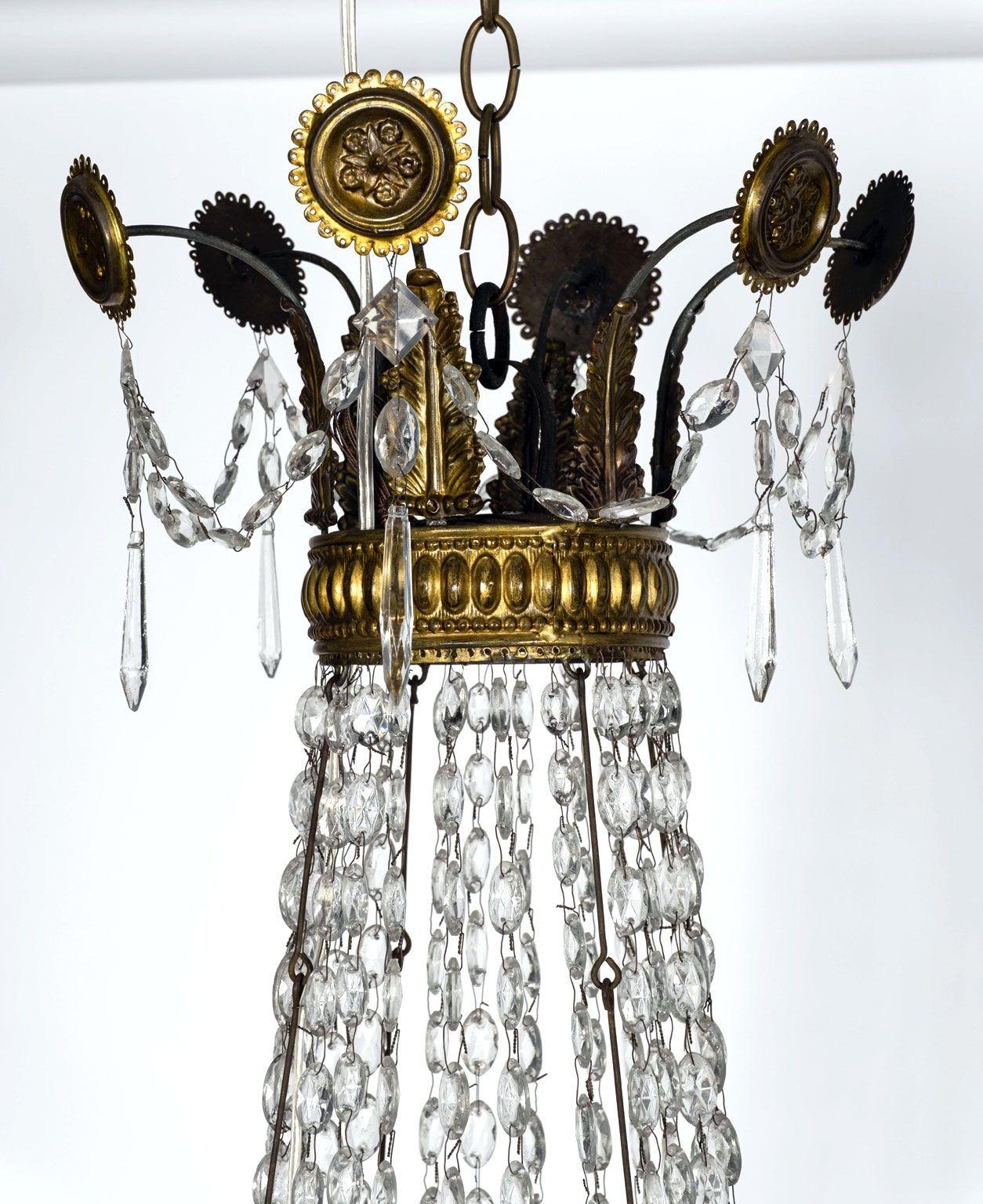 Gran araña imperio italiana de cristal y tole dorado circa 1815-1835. Anillos de repujado de tole dorado engarzados con cuentas de cristal y colgantes. Seis brazos de hierro dorado, cada uno de los cuales soporta una luz del tamaño de un candelabro.
