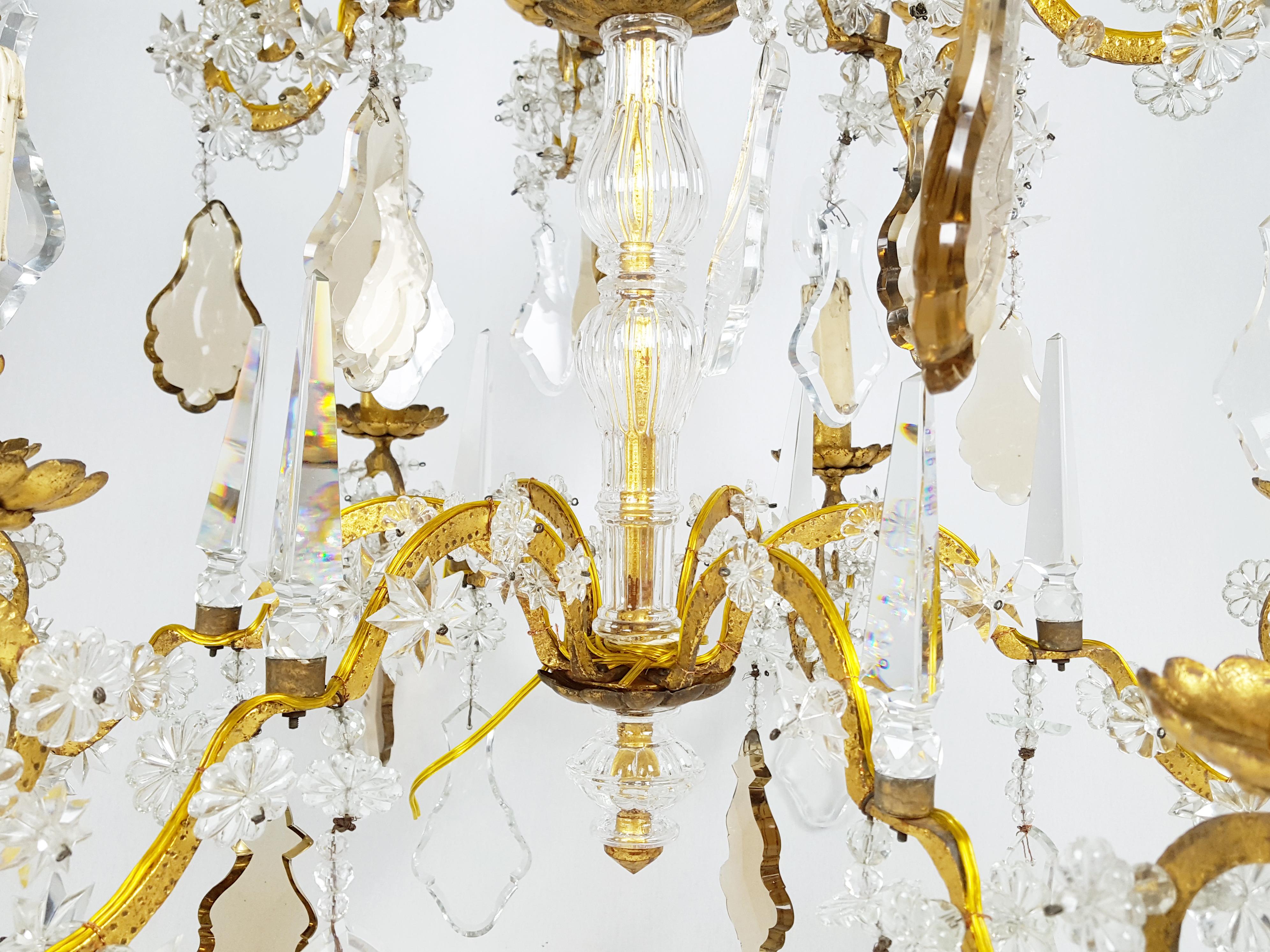 This large and fine 12-lights chandelier was manufactured in Italy in the 1930s. It consists of a golden leaf metal structure with different faceted crystal elements such as obelisks, stars, flowers and crystal drops. The golden leaf metal structure