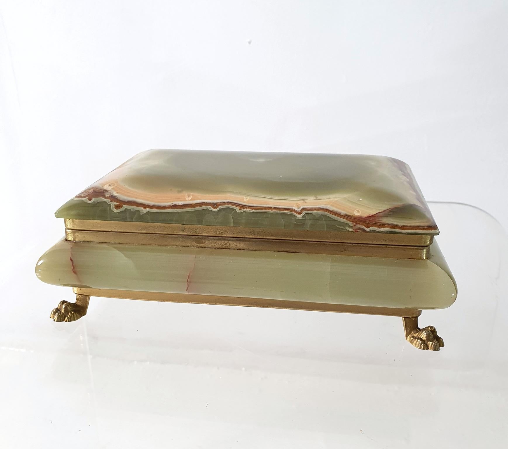 A large trinket or jewelry box with a hinged lid and made all in onyx and gilded feet. The onyx has a range of colors from red, brown, yellow and green.
