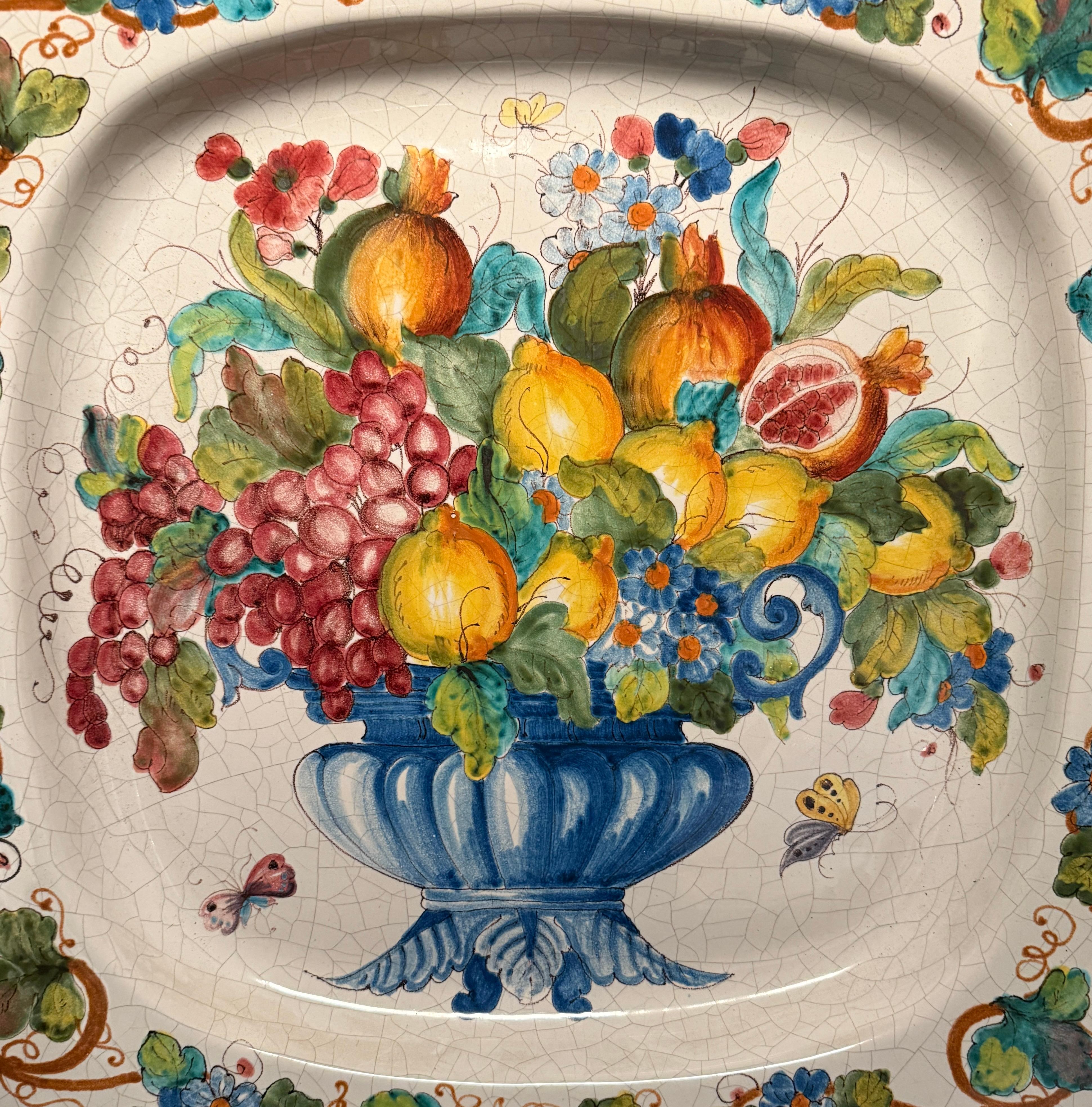 Grande vassoio/piatto in maiolica italiana di Armando Poggi, Firenze, Italia. Dipinto a mano decorato con un colorato fermo immagine di un'urna centrotavola piena di uva, foglie, fiori e frutti. Una bellissima decorazione per qualsiasi cucina o area