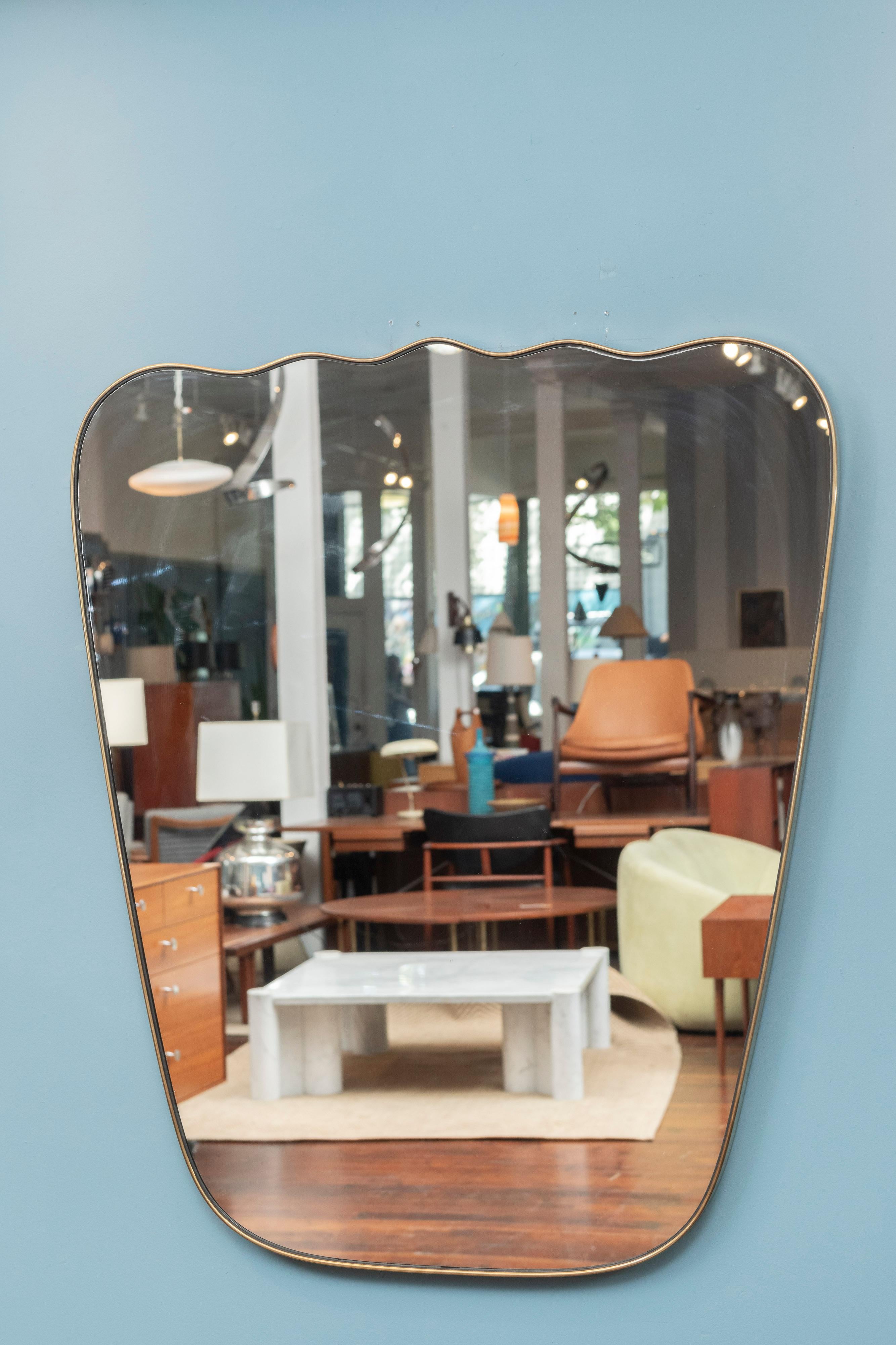 Miroir mural de style Mid-Century Modern italien fait sur mesure par les studios Adesso. Grand miroir impressionnant fabriqué avec des matériaux et un design de haute qualité, doté d'un cadre et d'une plaque de miroir élégants et fluides en laiton.