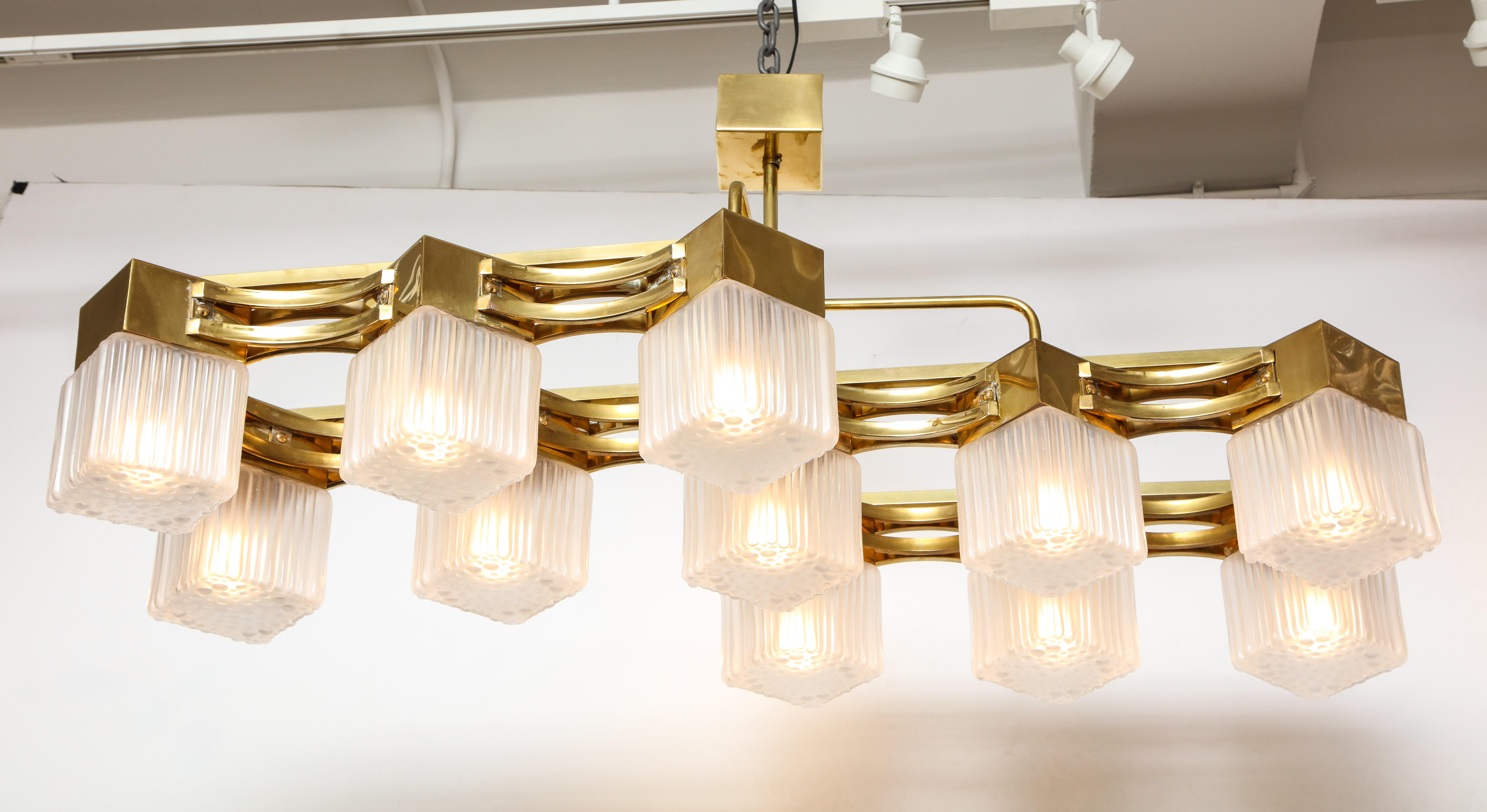 This Italian chandelier is the epitome of mid-century chic. Linear brass 11-arm frame features square, ridged, hand casted translucent white glass shades. Newly wired for U.S. standards. 

This chandelier is on display at the 1stdibs Gallery at