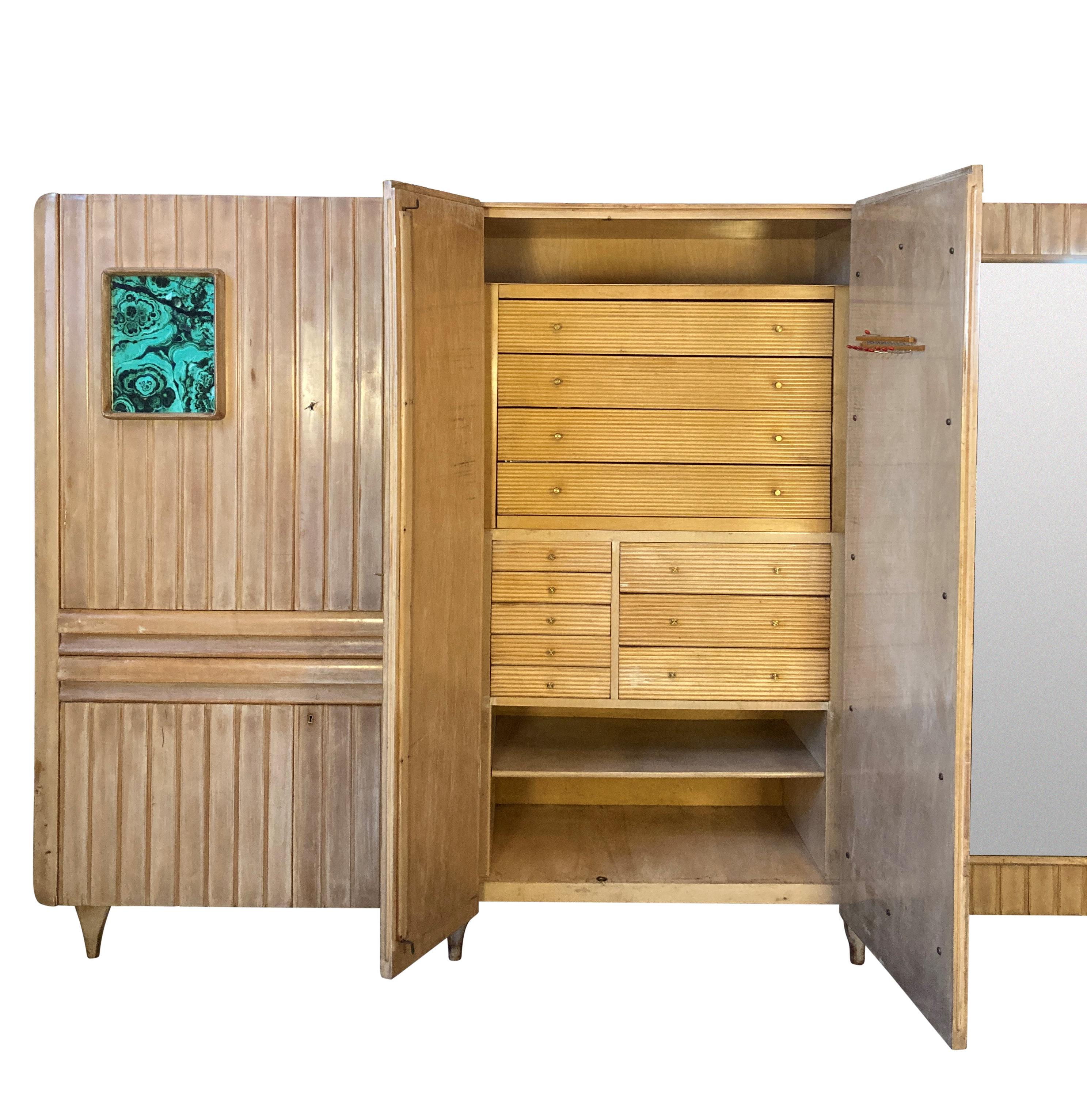 A large Italian Mid-Century segmented wardrobe in birch, comprising three sections, with hanging rails, shelves a drawers. With two mirrored doors and a faux malachite glazed panel. By Primo Giussani of Seregno.