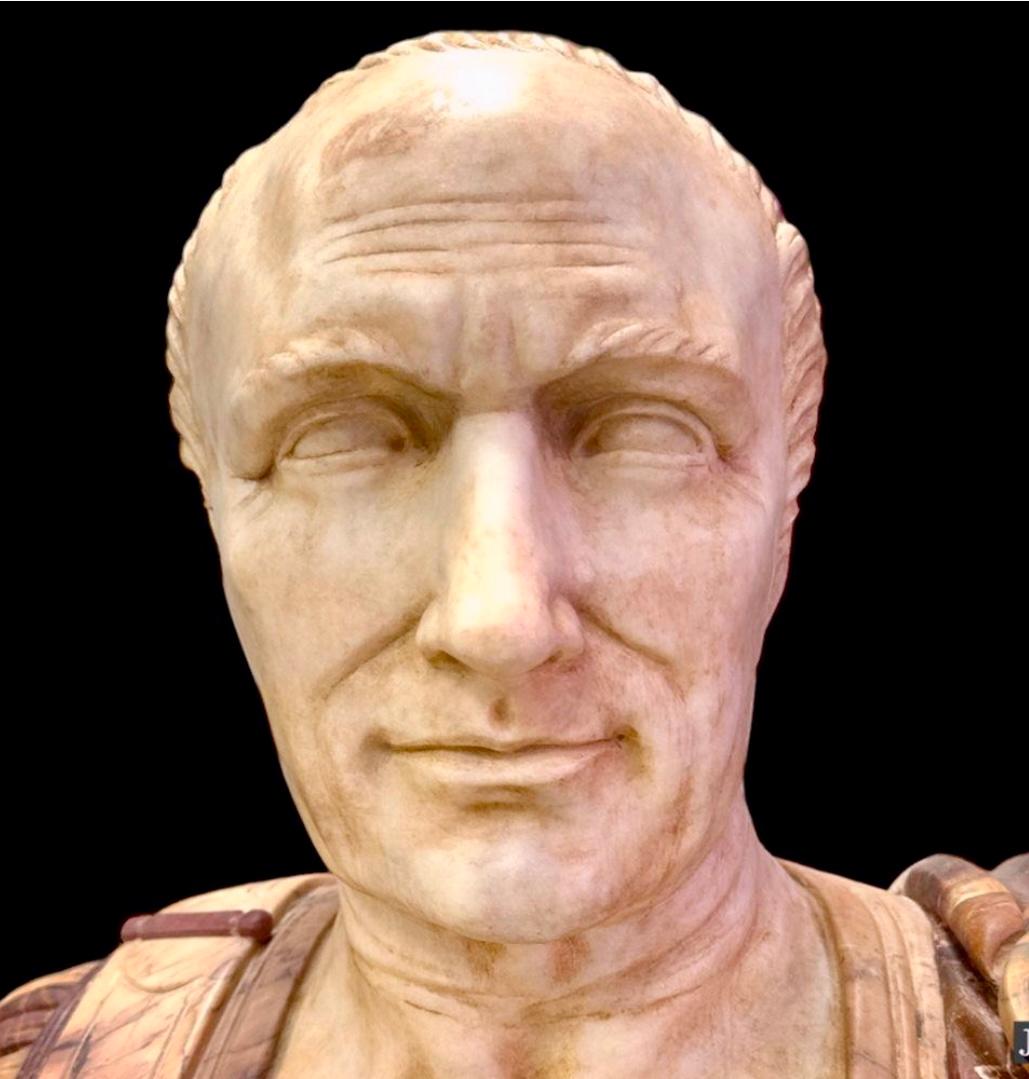 Eine große und beeindruckende Büste aus Marmor und Porphyr, die den Kaiser Julius Caesar darstellt. Der Kopf aus weißem Marmor ist in einen Torso aus Porphyr eingelassen, der mit verschiedenen Marmorsorten, darunter Siena und Onyx, auf einem Sockel
