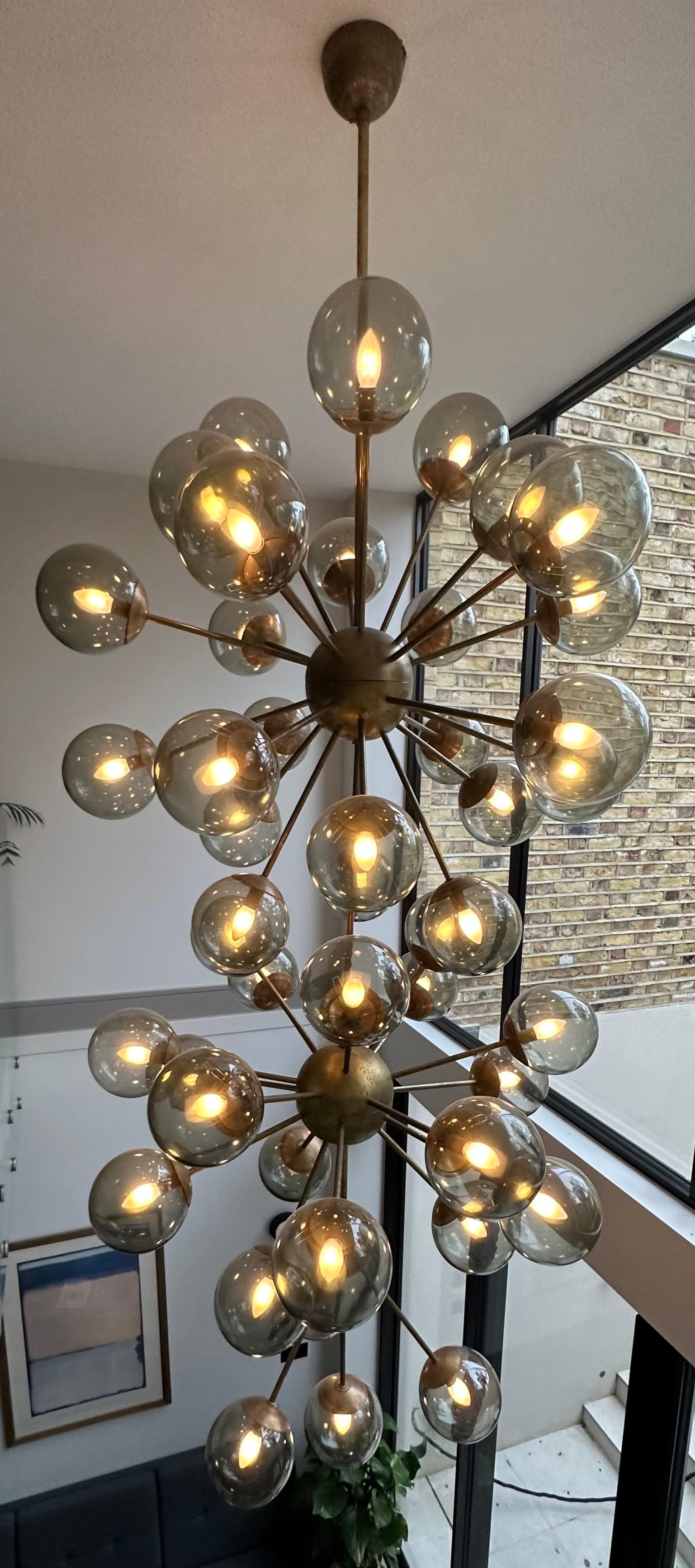 An amazing and quite spectacular space-age & futuristic 1980s Italian Murano glass globe & aged-brass sputnik chandelier.  Made in Italy.  The three inter-connected aged brass globes support each of the 48 arms with a smoked-green glass globe at