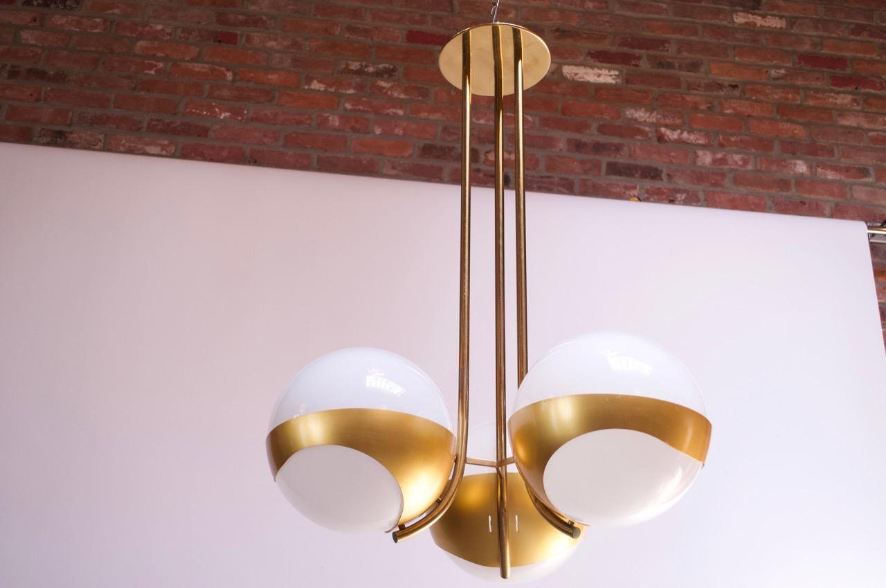 Impressive 1970s chandelier by Lamperti composed of three spherical milk glass shades housed in anodized aluminum 'cradles,' all supported by tubular brass stems / canopy. Elegant form and large-scale (40