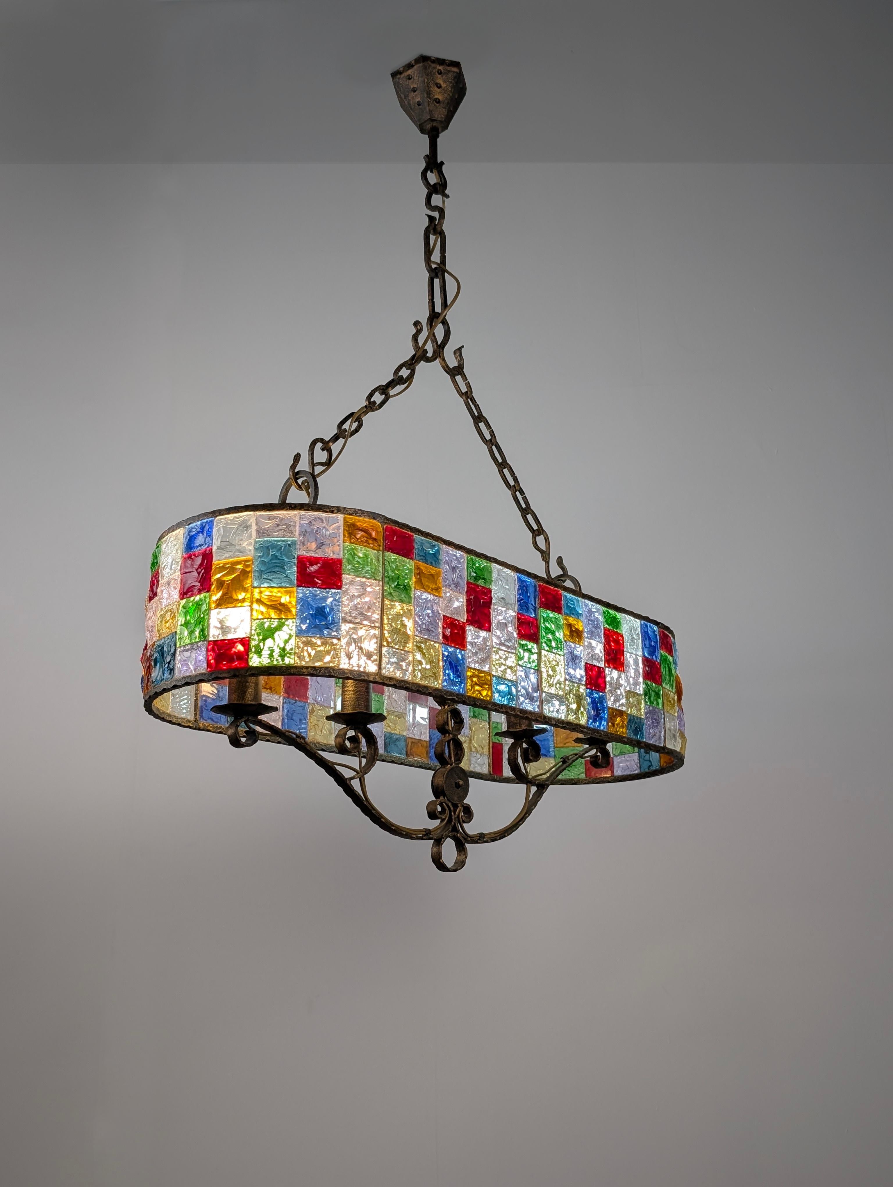 A large, Brutalist-style Italian chandelier made with beautiful, thick, hammered crystals of various sizes and colors, alongside a wrought iron structure. This elegant chandelier creates a beautiful atmosphere of lights and colors, playing equally