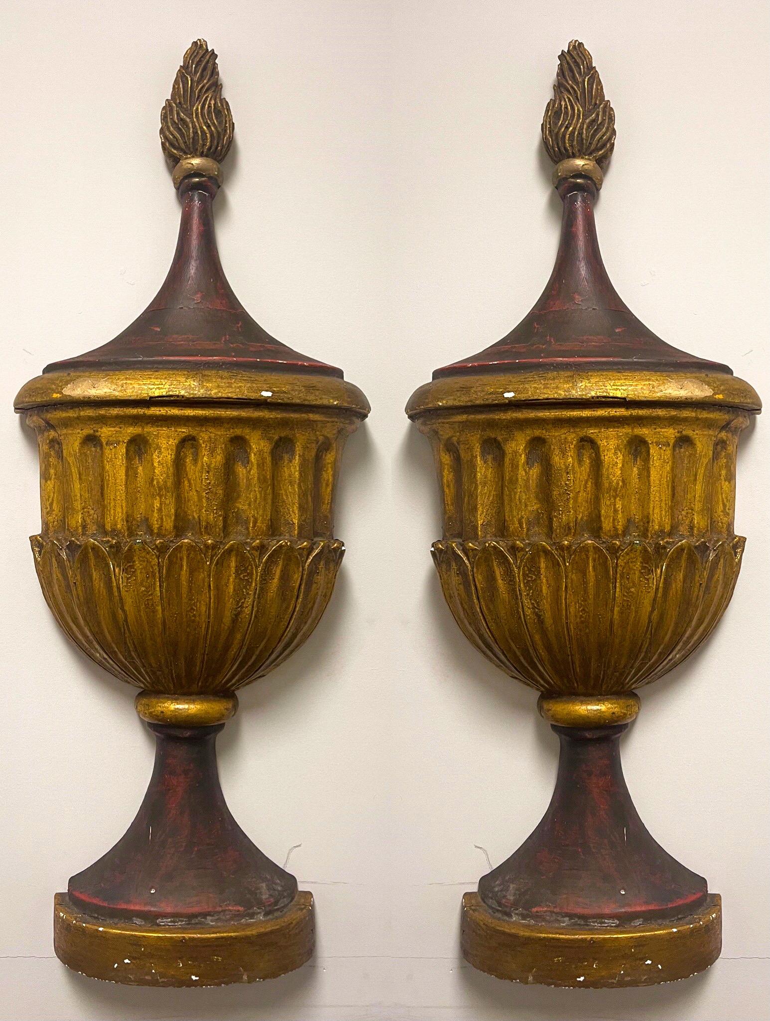 This is an incredible pair of wall mounted Italian neo-classical style urns. They appear to be gilded and painted gesso over cast plaster. They are large in scale and unmarked. The urns date to at least the middle of the 20th century.