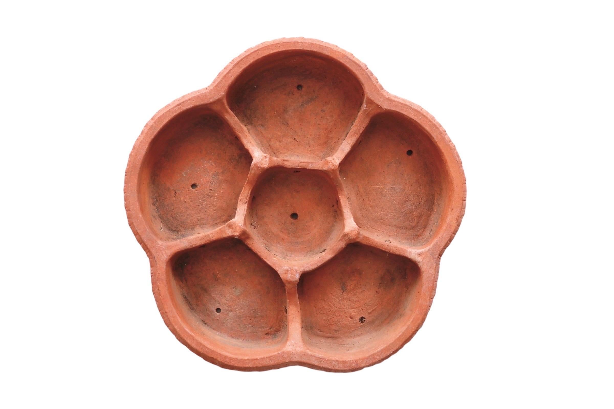 Grande soucoupe italienne, en terre cuite, en forme de quintefeuille. Décorée autour de la lèvre d'un motif en forme d'œuf et de fléchettes, avec des rosettes sur les côtés, la soucoupe comporte des cloisons pour six pots, chacun avec des trous de