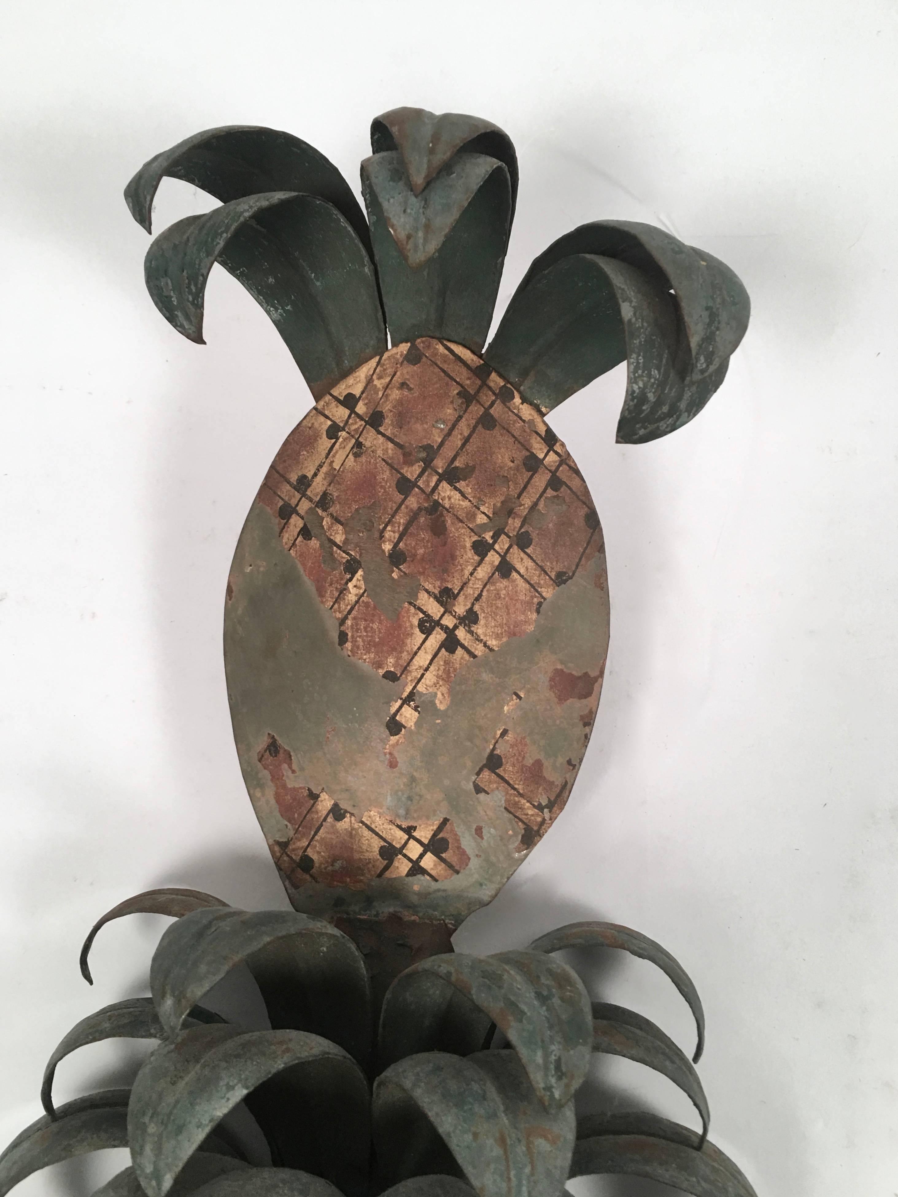 An unusual and stylish pair of large Italian tole (painted metal) pineapple plant sconces, each topped with a painted pineapple element over tiers of green curved leaves issuing from whimsically shaped and painted planters with scrolled sides. The