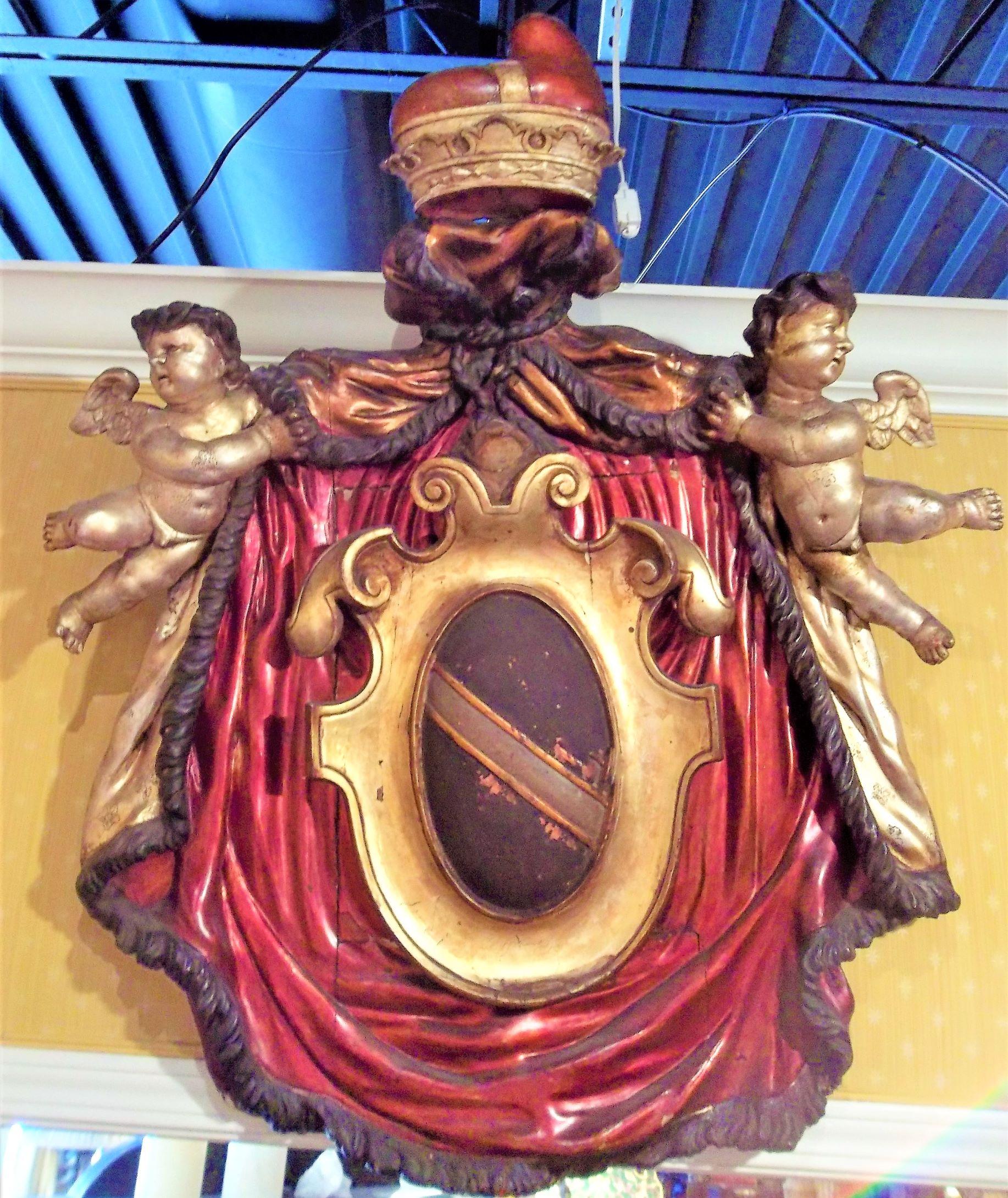 An antique carved Venetian armorial in the glassy enamel paint found on much Venetian furnishings .The cartouche shaped fringed ruby drapery being pulled apart by two silver gilt putti revealing the armorial. The drape outside in silver gilt and