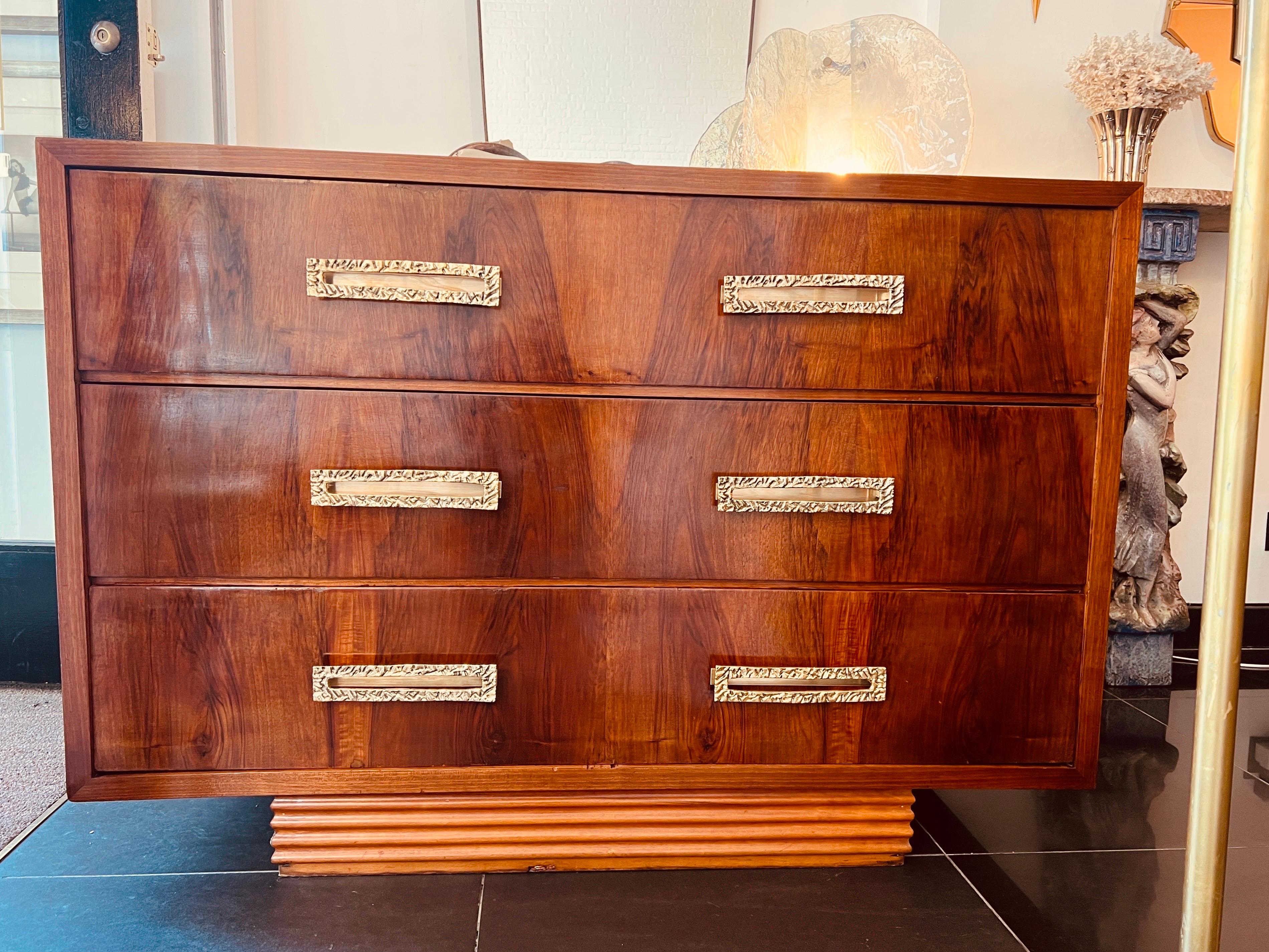 A beautifully designed three drawers walnut commode with hand-hammered solid brass handles standing on a rectangular reeded wood base. circa 1960s Italy.