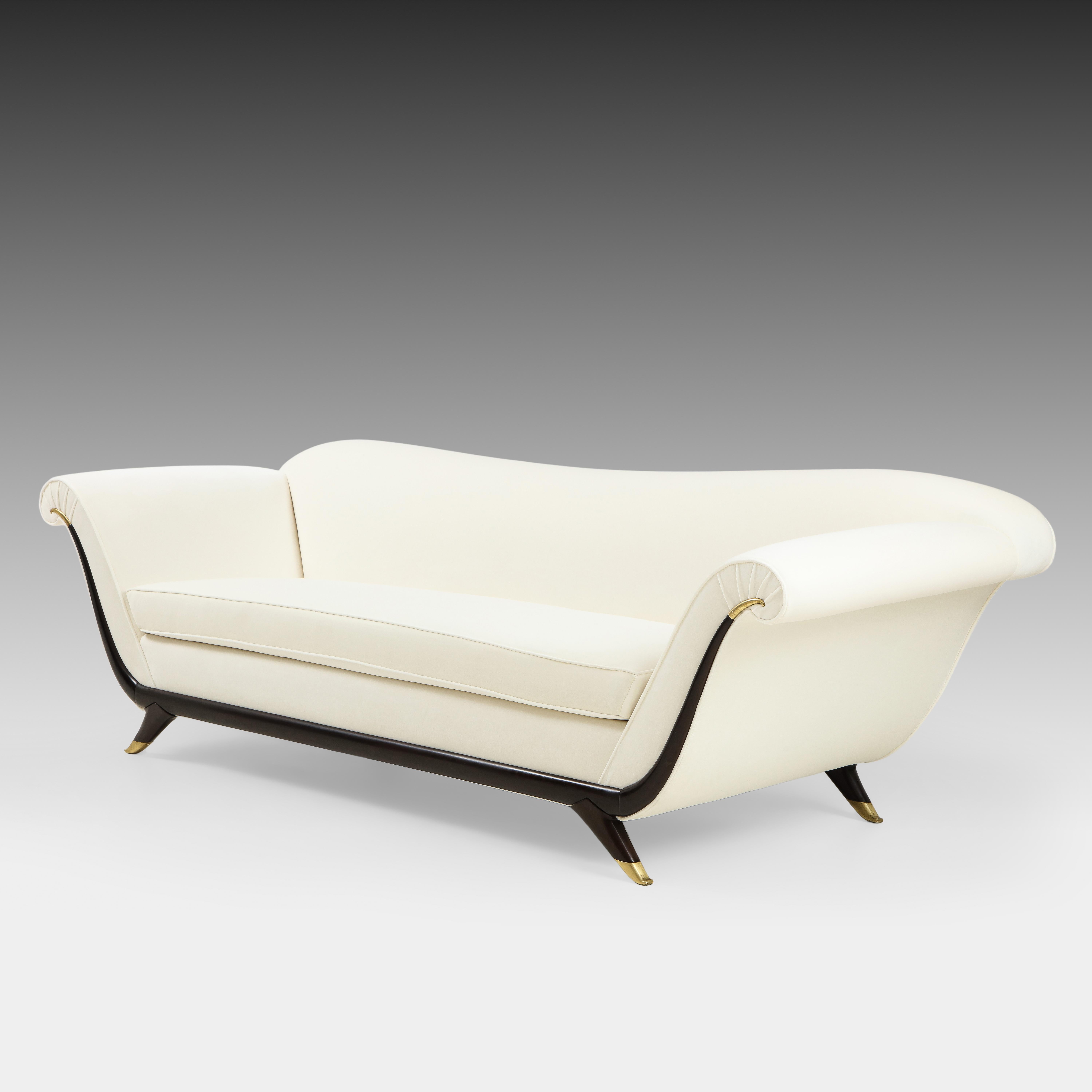 1940s Italian elegant and classic upholstered sofa with single seat cushion, lacquered wood and brass details, and splayed legs ending in brass sabots attributed to Guglielmo Ulrich. This exquisite gondola-shaped sofa is contoured with sweeping
