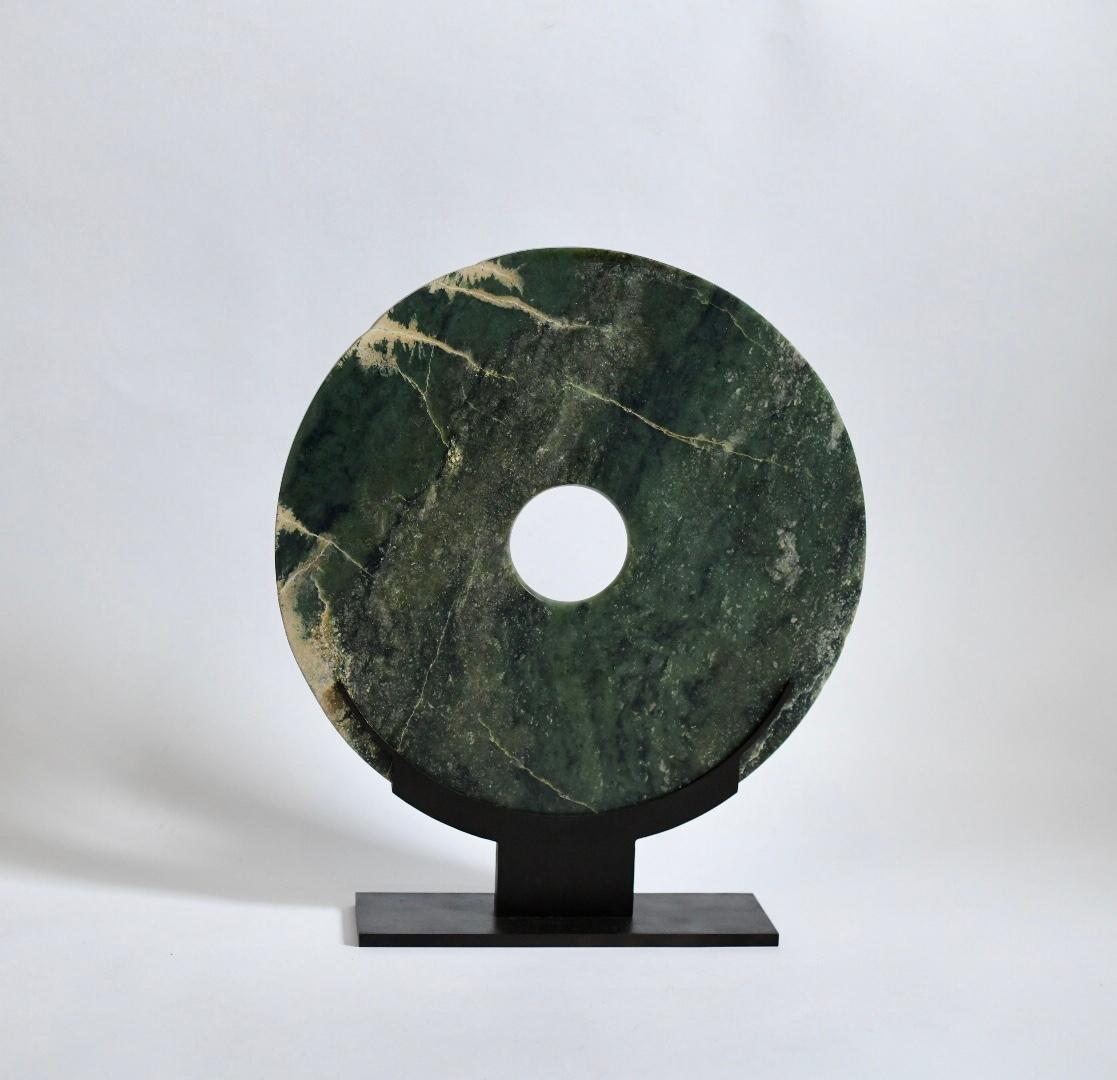 A large jade disc with veins. Antique brass stand.