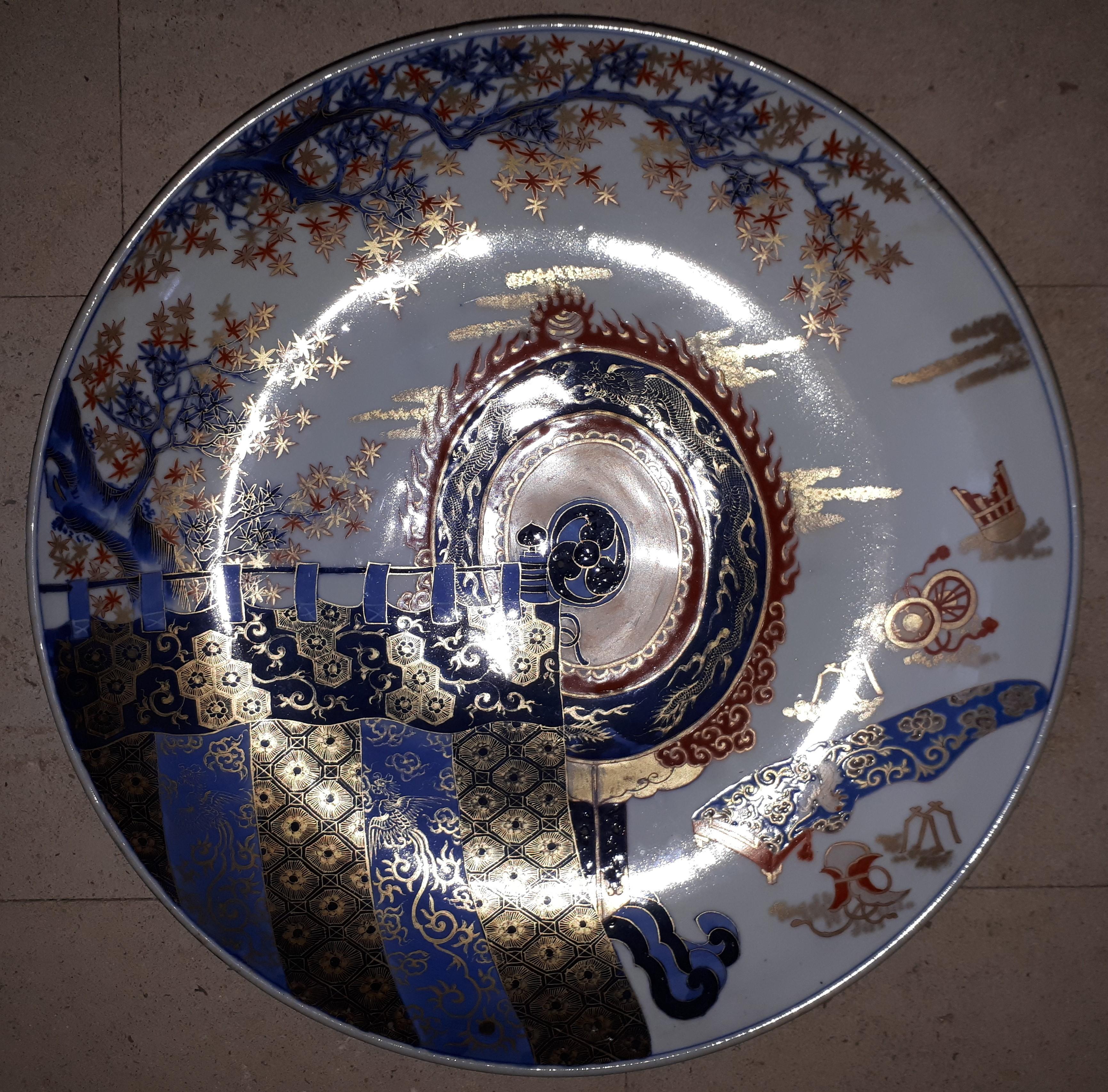 Large Arita porcelain dish, with polychrome decoration and gilt highlights of standards placed under a maple tree.
Japan, late 19th century.