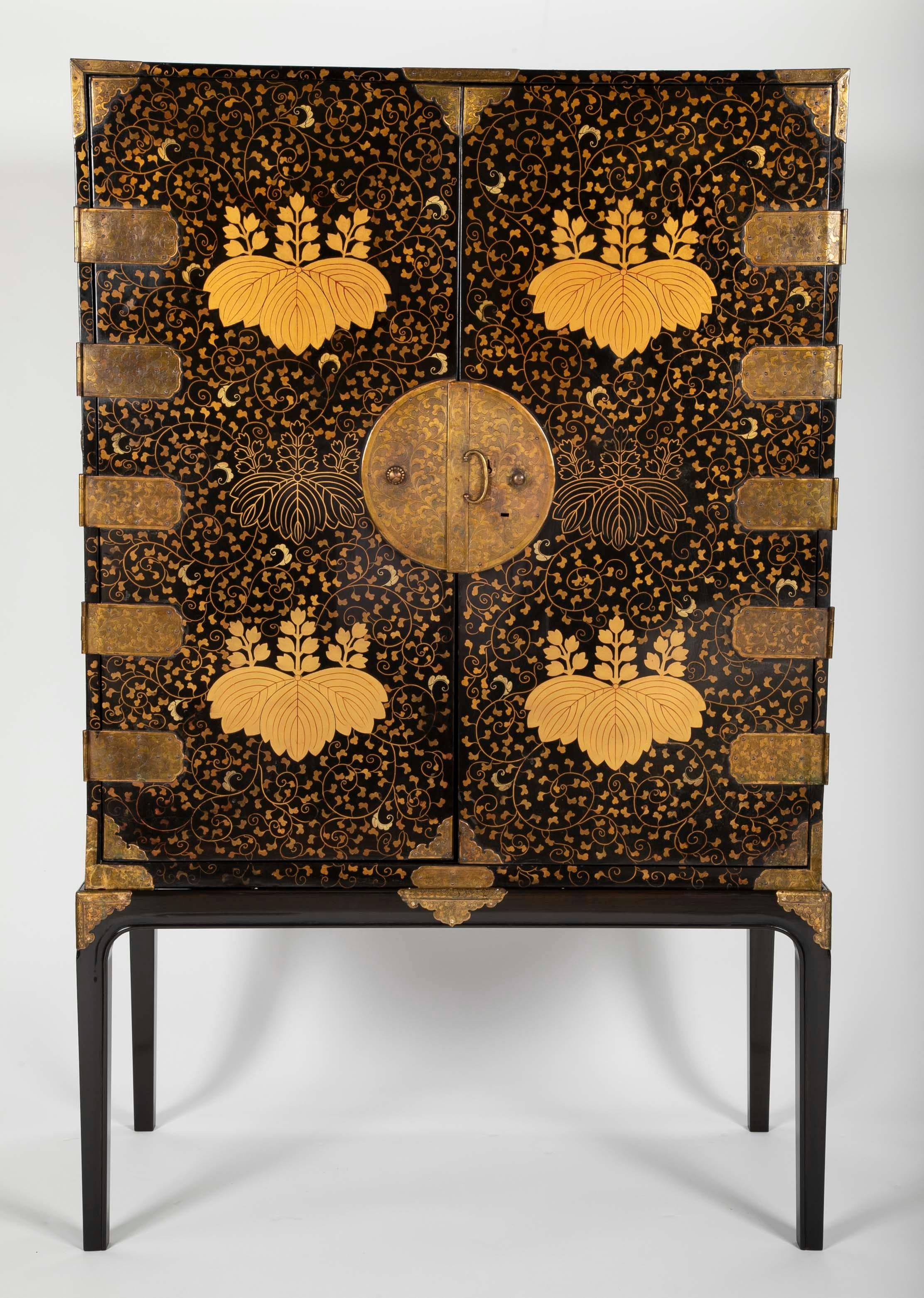 A large Japanese black and gold lacquered cabinet with Toyotomi mon and vine decorations. Mounted with gilt and etched bronze hardware. Later stand also mounted with period hardware. Drawers lined with Japanese paper depicting clouds and one