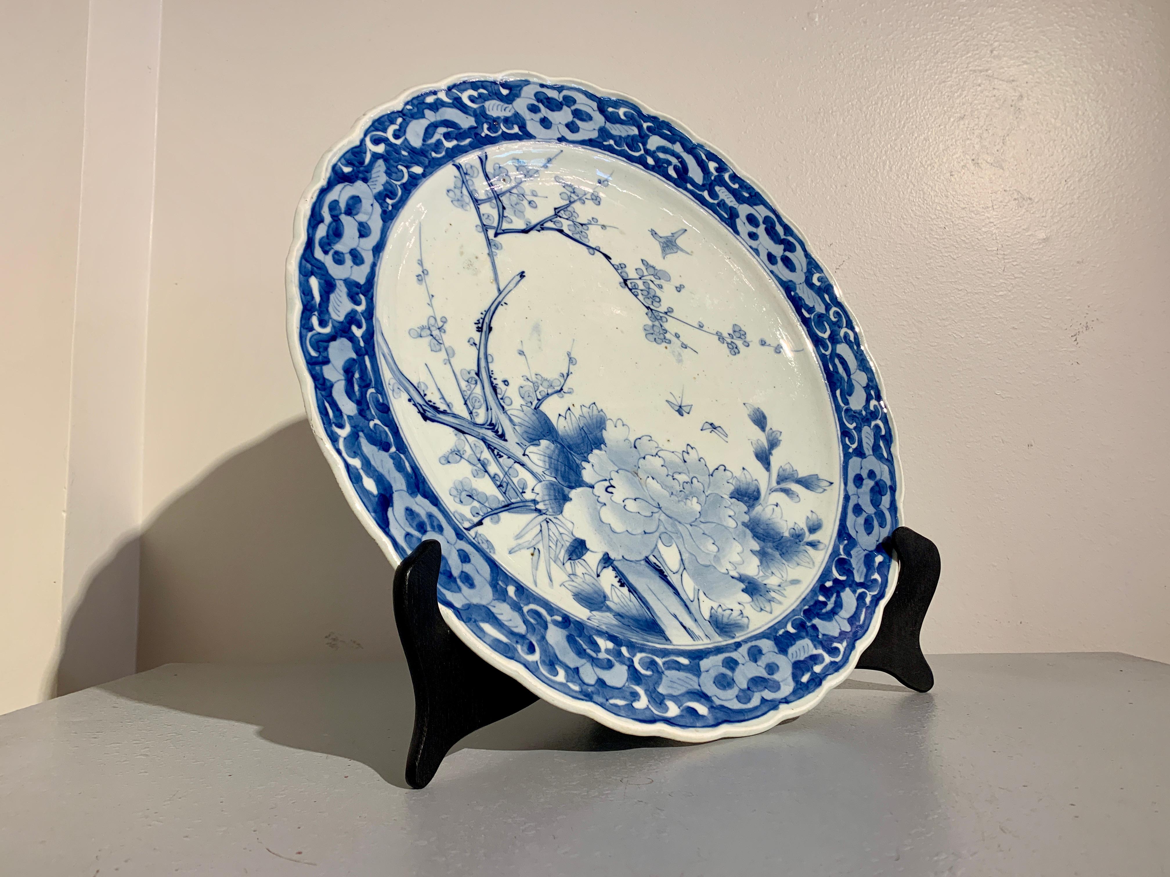 A fine and large antique Japanese porcelain blue and white decorated Arita ware charger with scalloped rim, Meiji Period, mid to late 19th century, Japan.

The large charger features a large peony blossom with flowering cherry in the background. A