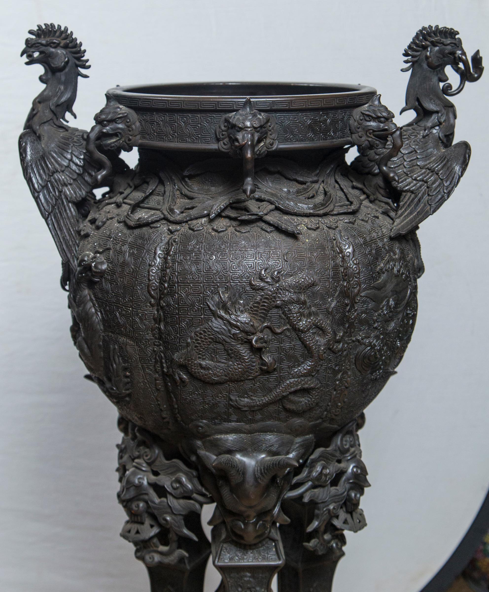 Dating from the Meiji period this standing koro or  incense  burner has a circular stepped base. Three legs topped with horned and other demons standing on upside down foo dogs. Elephant heads on the rim and phoenix birds, wing spread, upper