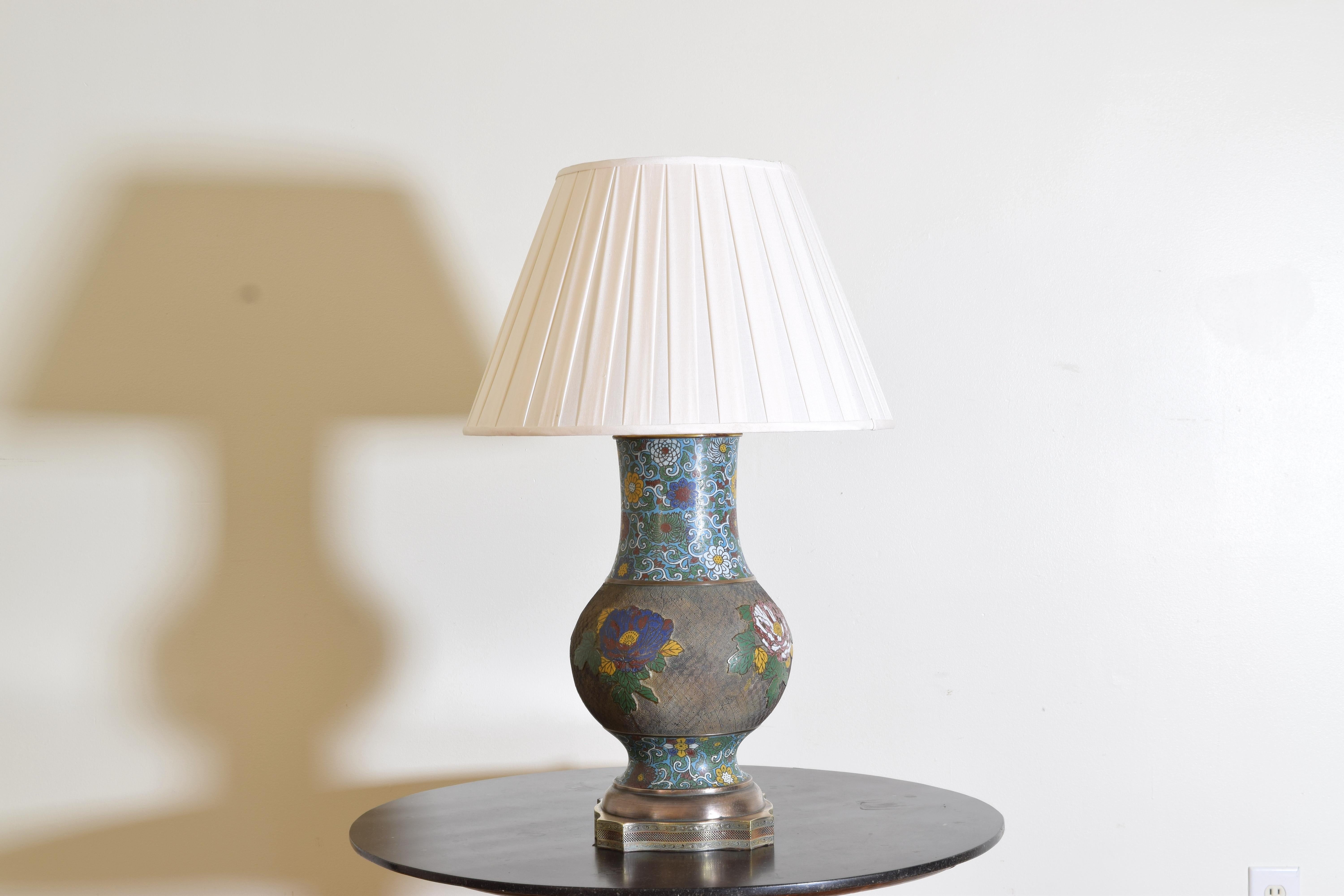 The textured brass body with enameled flowers and raised on a decorative pierced brass base, height is measured to top of silk pleated shade, height of lamp is 20 inches.