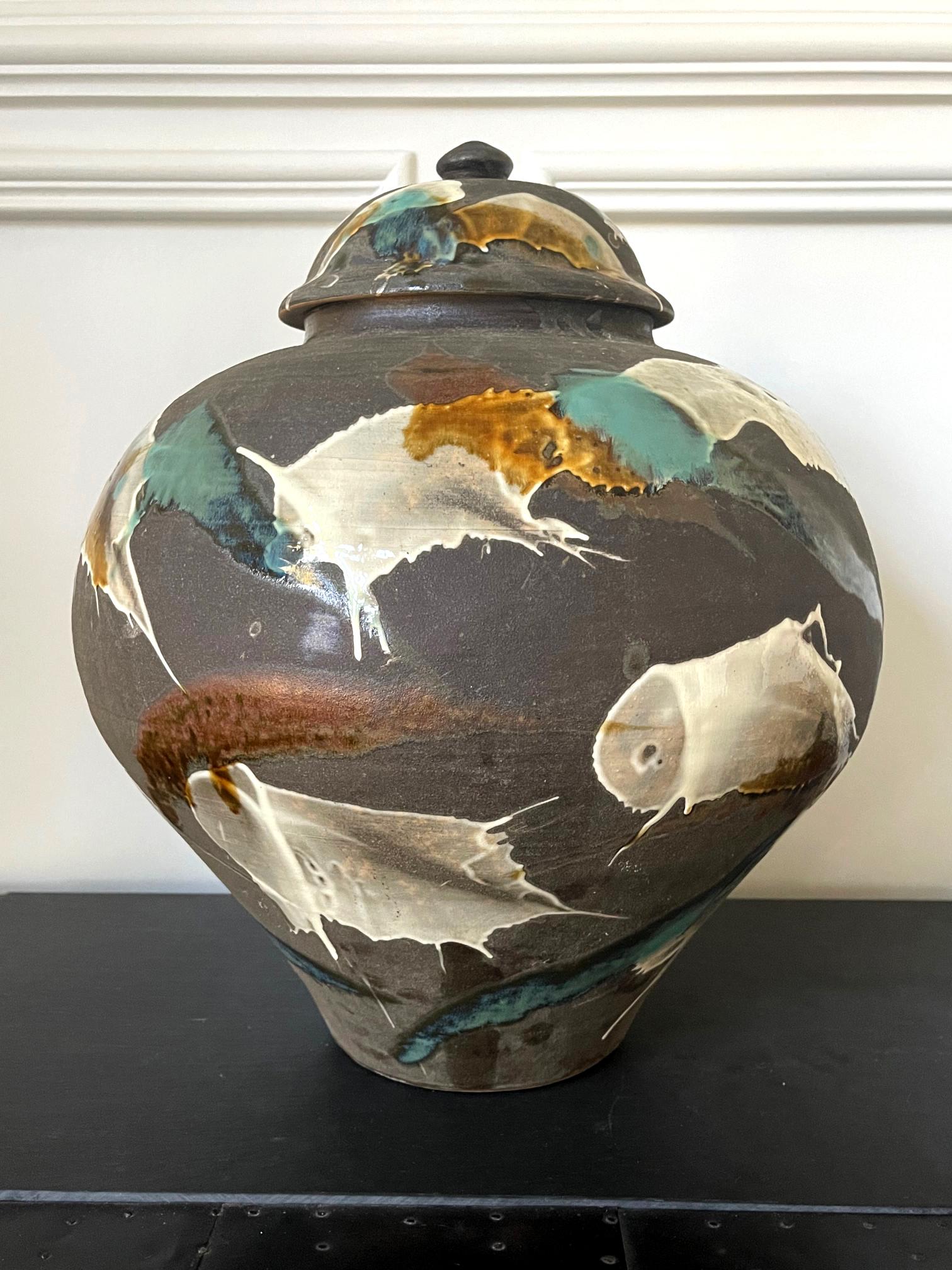 A large Japanese lidded ceramic jar from the kiln of Onda Yaki, circa 2010. The stoneware jar impresses the viewer with a robust bulbous form. Its black body is nearly unglazed but exuberantly splashed with strokes of slip glazes of white, yellow