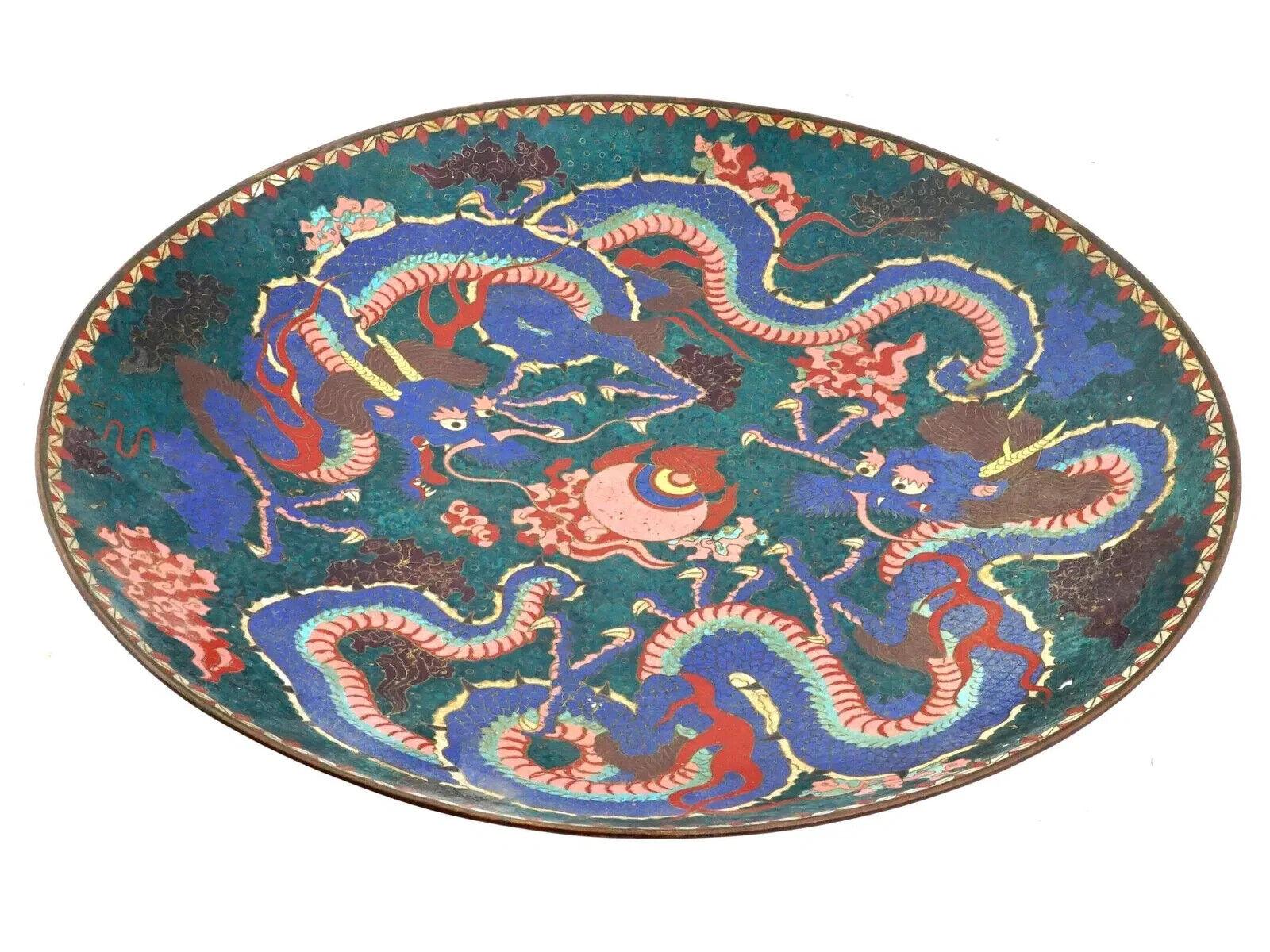 A large Japanese enamel plate charger. The plate is enameled with a polychrome design representing a pair of dragons surrounded by fire and cloud motifs made in the Cloisonne technique. The backside is adorned with floral, foliage, foliate scroll