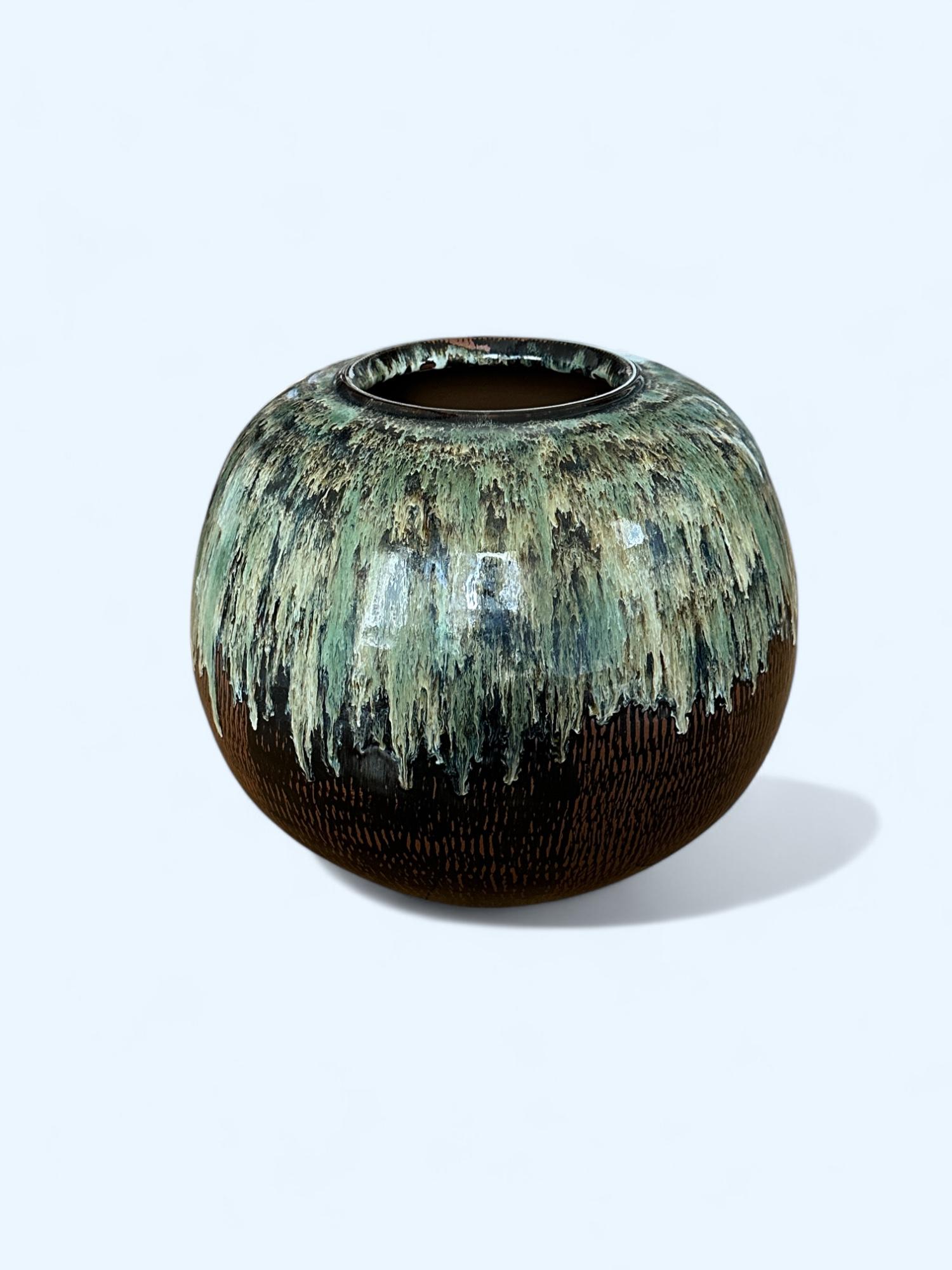 Ce vase japonais remarquable présente une épaisse glaçure cendrée en cascade dans de riches tons de vert céladon et d'ivoire sur un corps brun profond avec des motifs verticaux sculptés. La glaçure s'écoule de façon dynamique à partir du haut,