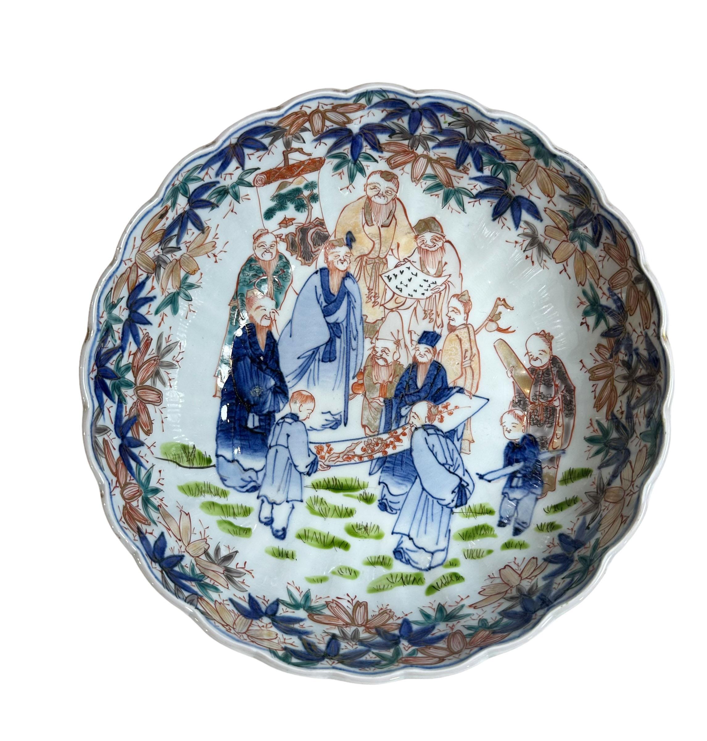 A large Japanese Imari bowl with mini figures reading scrolls. It is an immaculate condition has a fluted edge with more of the oriental people on the bottom of the bowl. Circa 19th century.