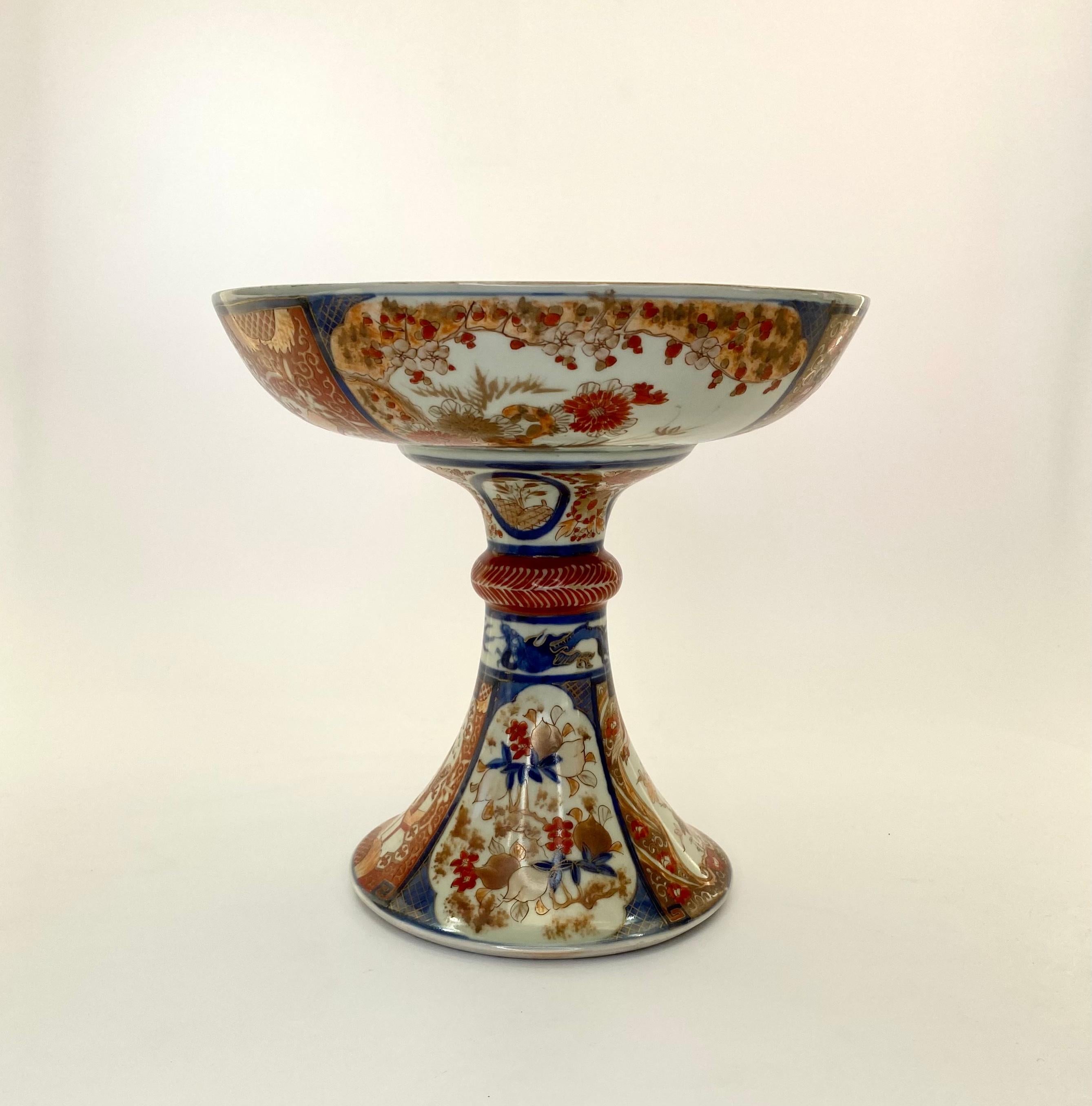 
An unusual Japanese Imari porcelain stand, Arita, c. 1890. Meiji Period. The large bowl, painted with a roundel, containing a coiled dragon, within a continuous band of stylised flowers heads. The rim with a broad band of panels containing peaches,