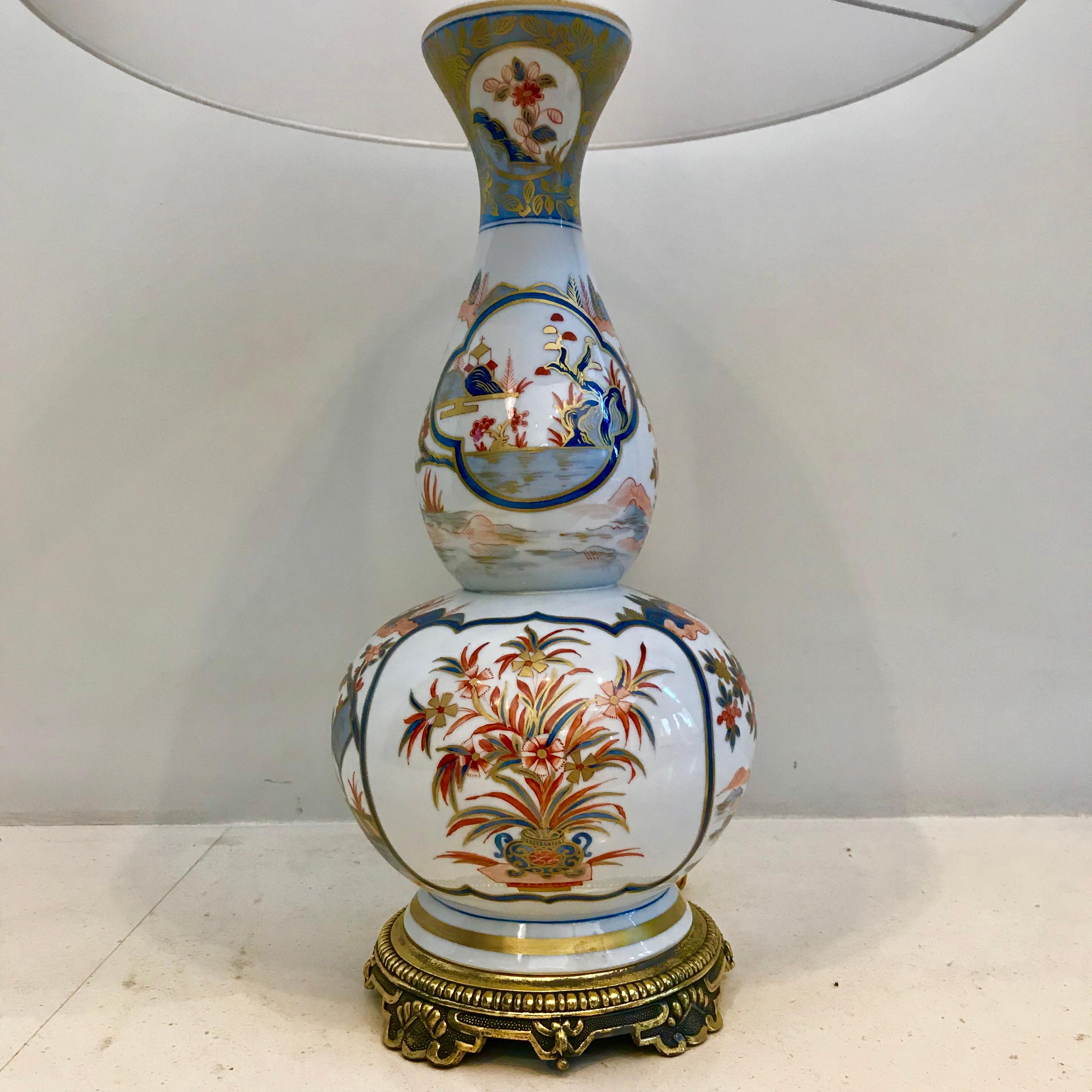 Antique double-gourd hand painted Imari porcelain table lamp having the classical blue, red and gold colors. With a garden scene and flowers in blue vase. The upper and bottom part is nicely brass-mounted.