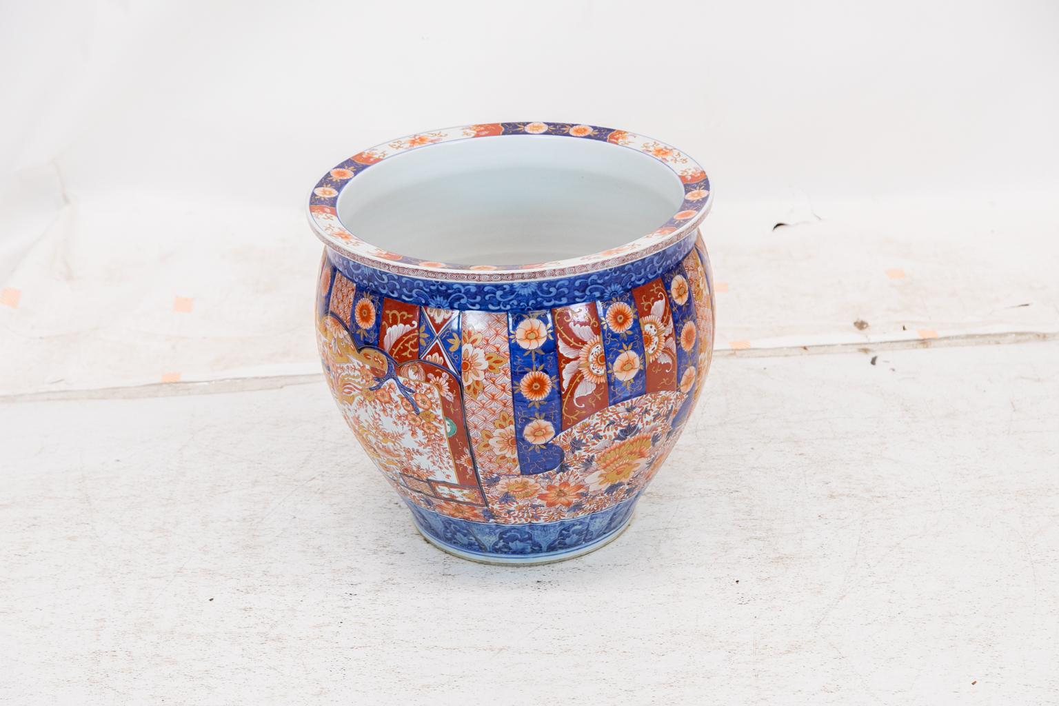 This unusually large Imari jardinière has central cartouches with birds, trees, and flowers with extensive gold highlights. The top and base have blue and white floral bands. The top rim has blue, white, and red floral decoration with gold