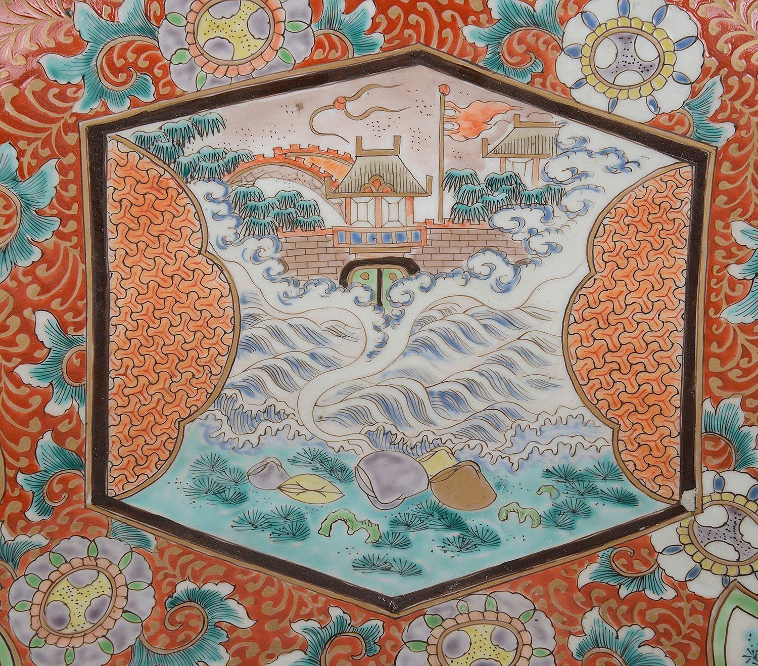 A large late 19th Century Japanese Imari porcelain circular charger, having wonderful bold orange colouring to the ground, with scrolling foliate decoration, inset hand painted panels depicting Pagoda buildings, waves, and birds flying among blossom