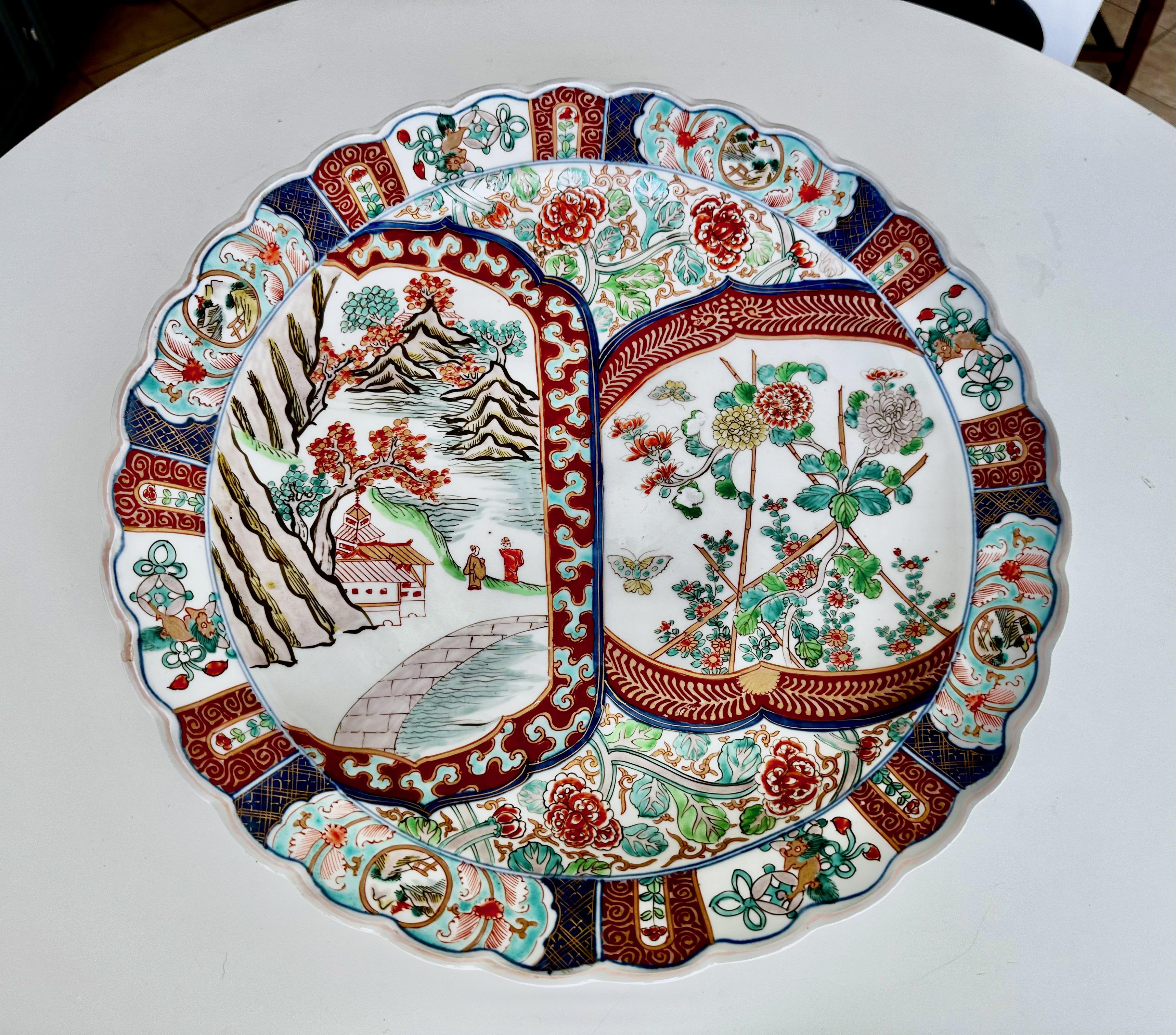 Hand painted porcelain Japanese Imari charger scallop edge plate with figures, buildings, trees, mountains, birds and floral design.