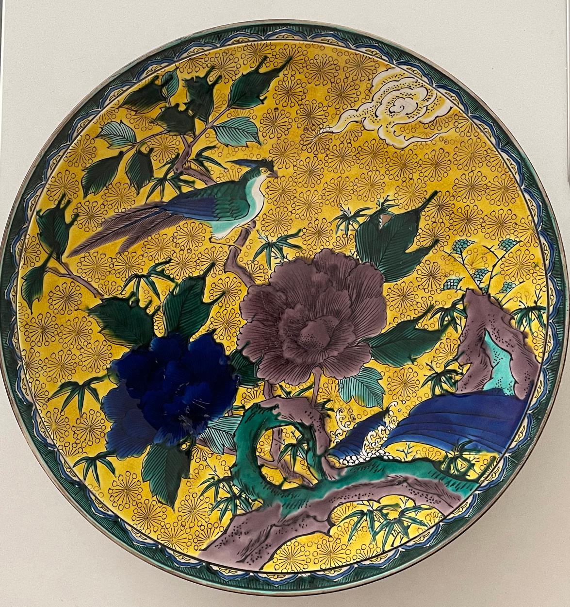 Rare chargeur en céramique japonaise à fond jaune de 15,5 pouces de diamètre.

Décorée sur une base jaune d'un oiseau, de feuillages et de fleurs dans des tons jaunes, bleus, bruns et verts.

Signé sur la base avec le cachet du studio.

En