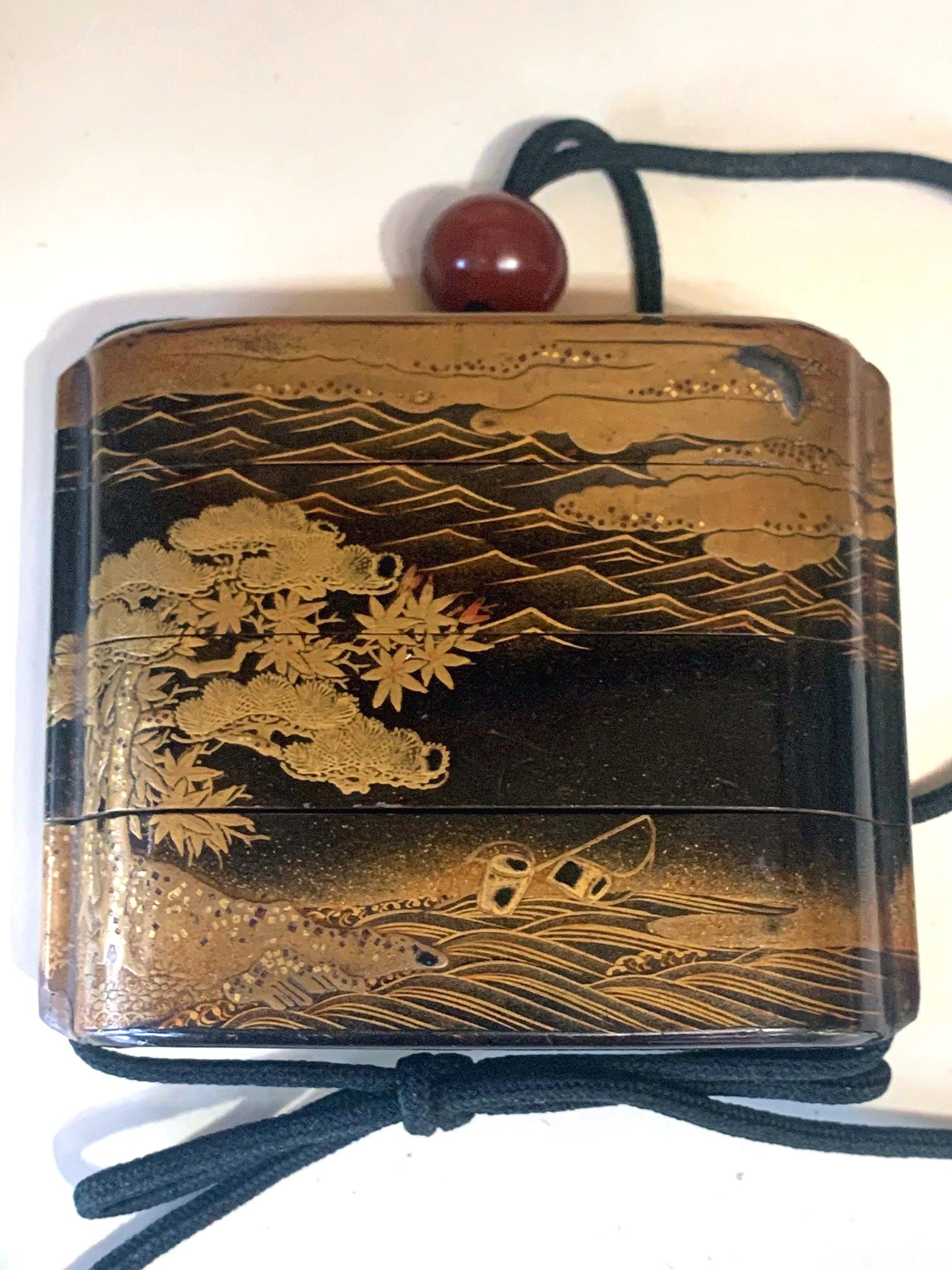 A Japanese four-case inro with string and an amber bead ojime of Meiji period circa 19th century. The relatively large inro has a black lacquered background with fine detailed gold hiramaki-e decoration. On one side, a cluster of three huts stand