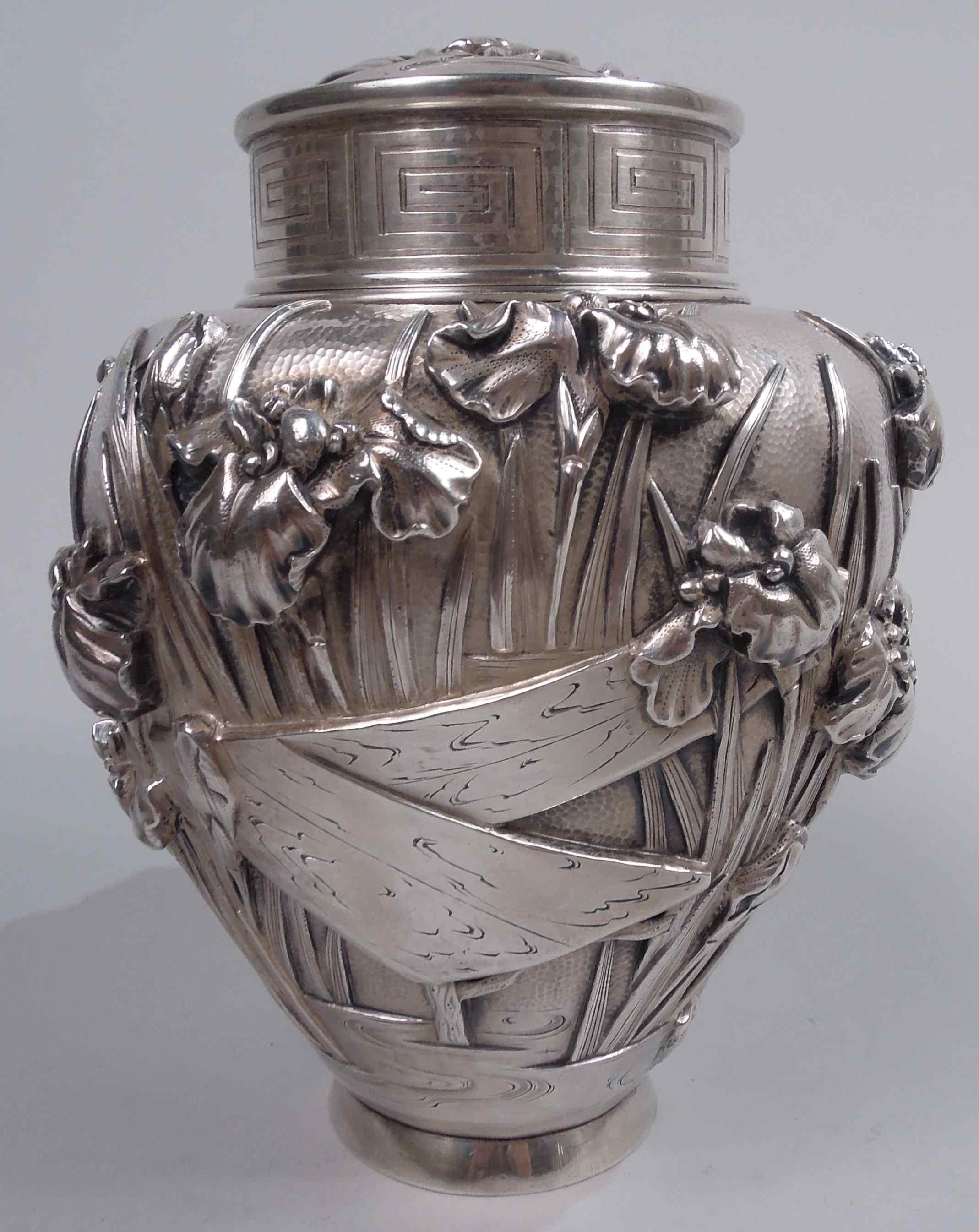 Japanese silver tea caddy, ca 1890. Ovoid; plain splayed foot and short neck and short inset neck. Applied and chased irises with floppy, irregular petals and reeded tendrils rooted in eddying water as well as baskets and wood staves; hand-hammered