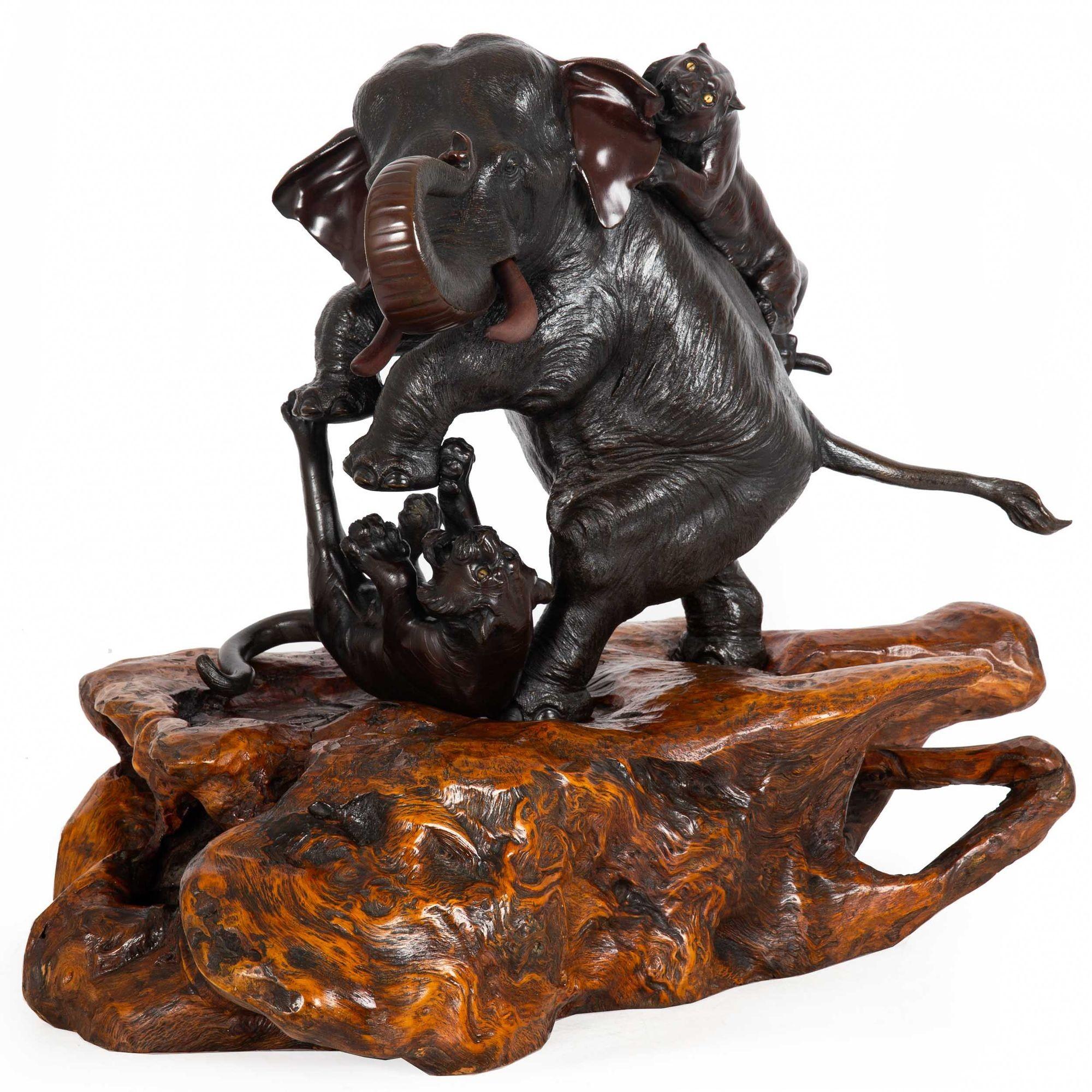 MEIJI PERIOD BRONZE OKIMONO OF ELEPHANT BEING ATTACKED BY TWO TIGERS
Workshop of Omori Mitsumoto (kôgen), 大森光元, Japan, circa 1900

Cast and patinated bronze, hardwood base, two carved hardwood tusks, glass eyes in tigers  signed to the underside of