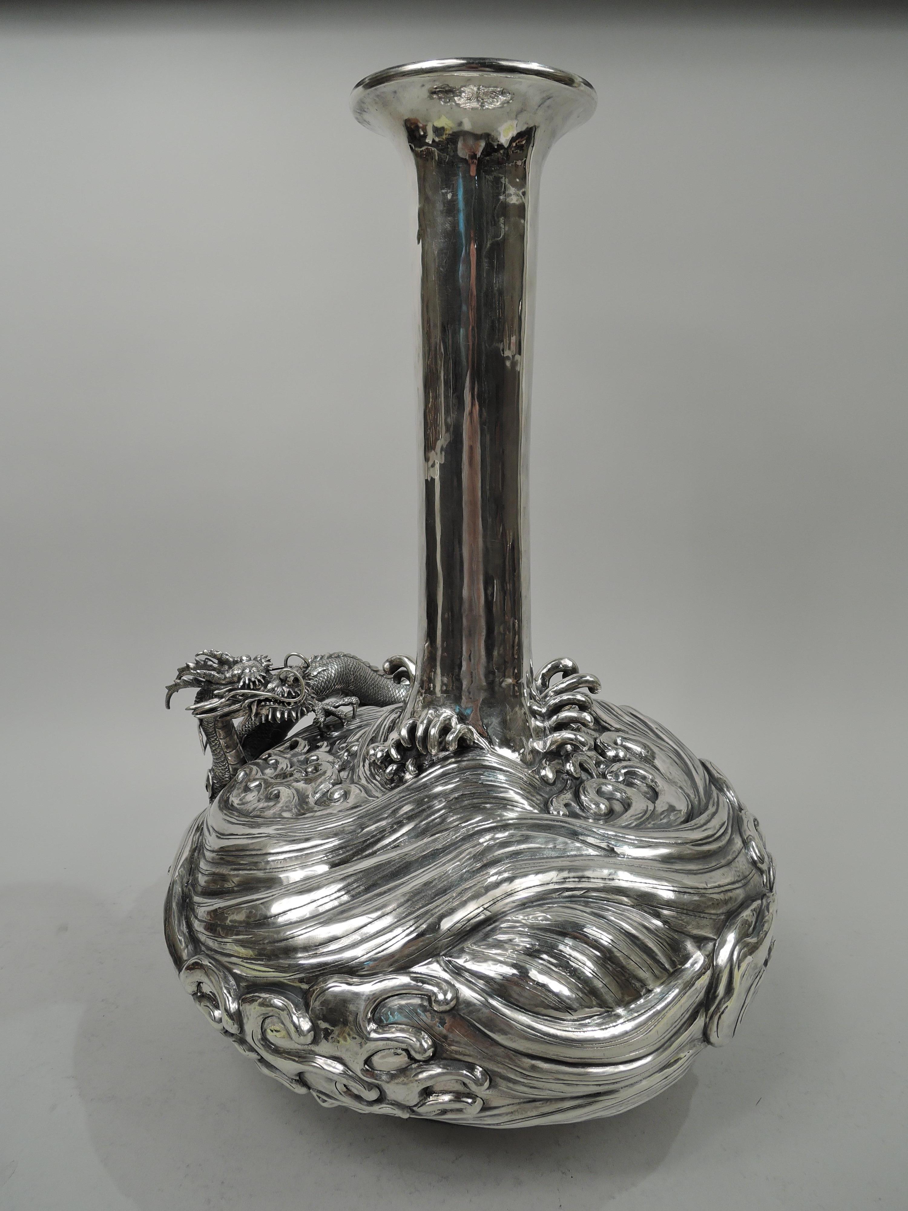 Dramatic Japanese Meiji silver centerpiece vase, ca 1900. Globular bowl with tall cylindrical neck and flared mouth; raised and inset foot. Bowl has wraparound roiling waves with claw-like spume in relief and a horned and scaley dragon, baring teeth