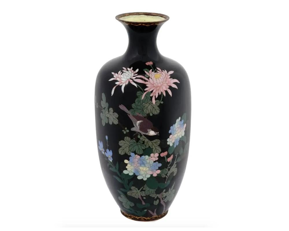 A large antique Japanese Meiji period enamel over brass vase. The vase has an amphora shaped body and a narrow neck. The ware is enameled with a polychrome image of a bird in blossoming flowers made in the Cloisonne technique on black ground.