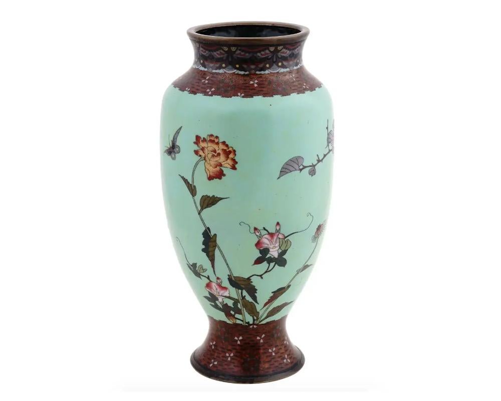 A large antique Japanese late Meiji period enamel over brass vase. The vase has an amphora shaped body and a wide neck. The ware is enameled with a polychrome image of birds in blossoming cherry flowers made in the Cloisonne technique on light green